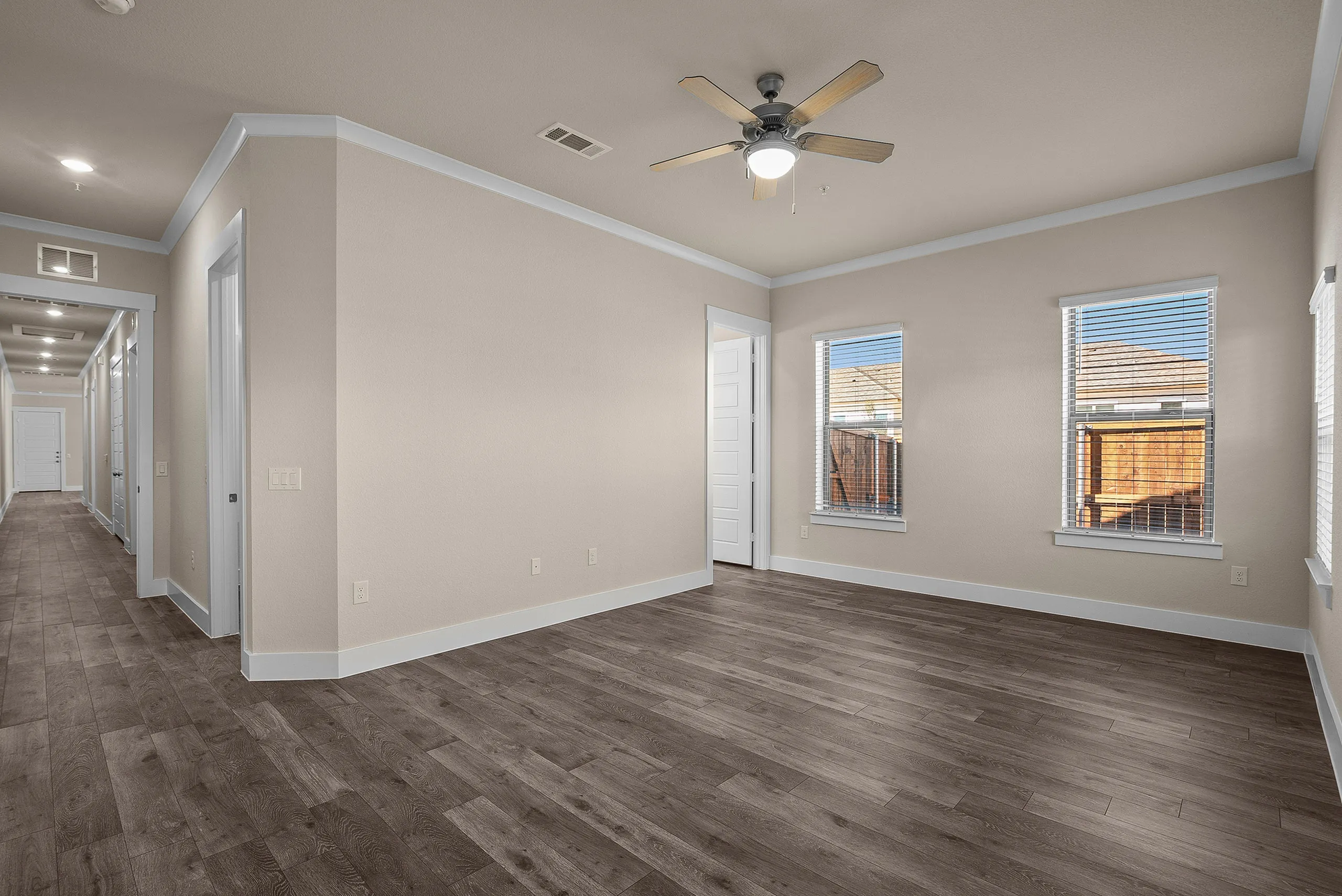 Contemporary living space with elegant wood flooring, large windows for natural light, and tray ceiling with fan.