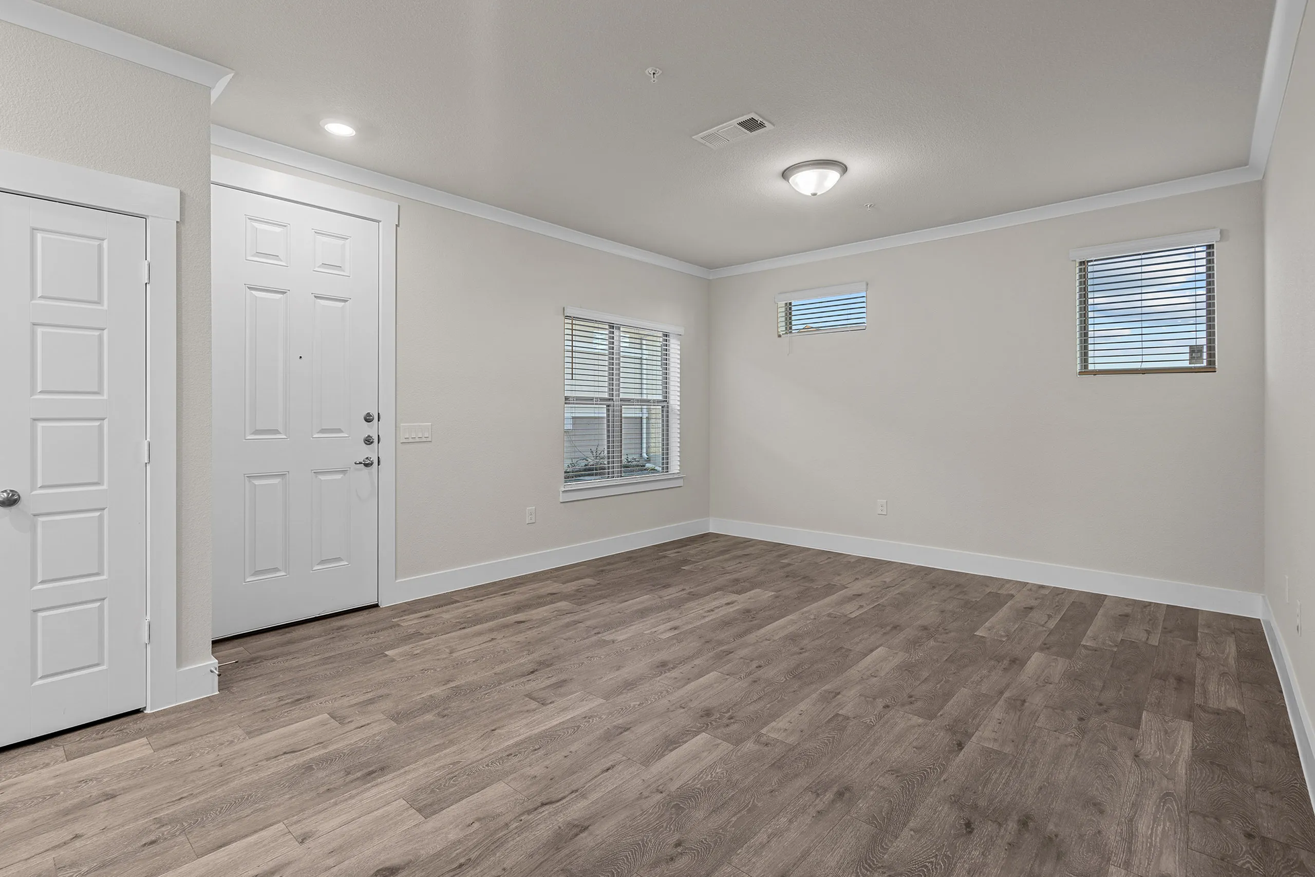Modern apartment interior with pristine white walls, wood-style flooring, and ample natural light from large windows.