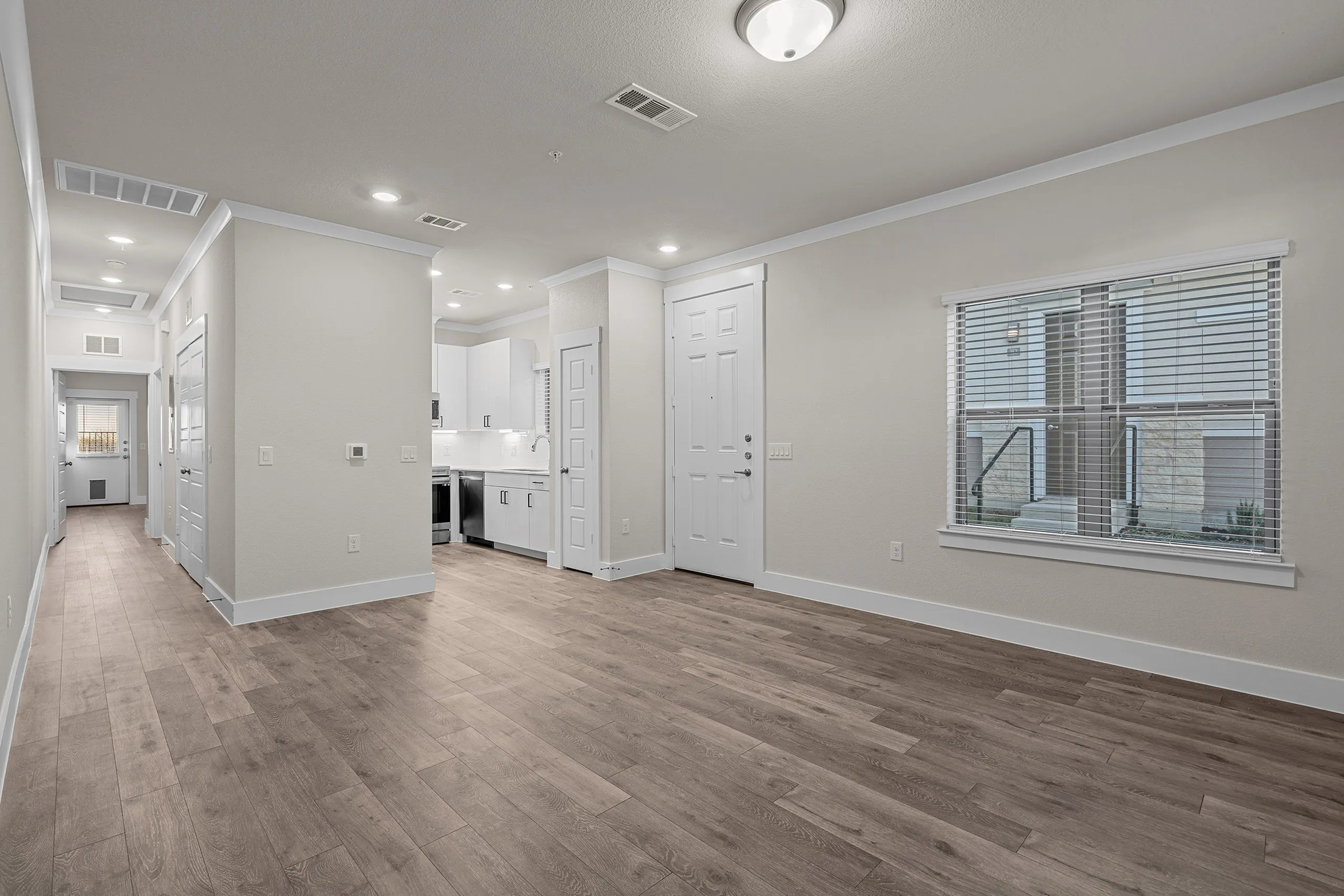 Bright and spacious living area with modern kitchen, featuring sleek white cabinets, stainless steel appliances, and elegant wood flooring.