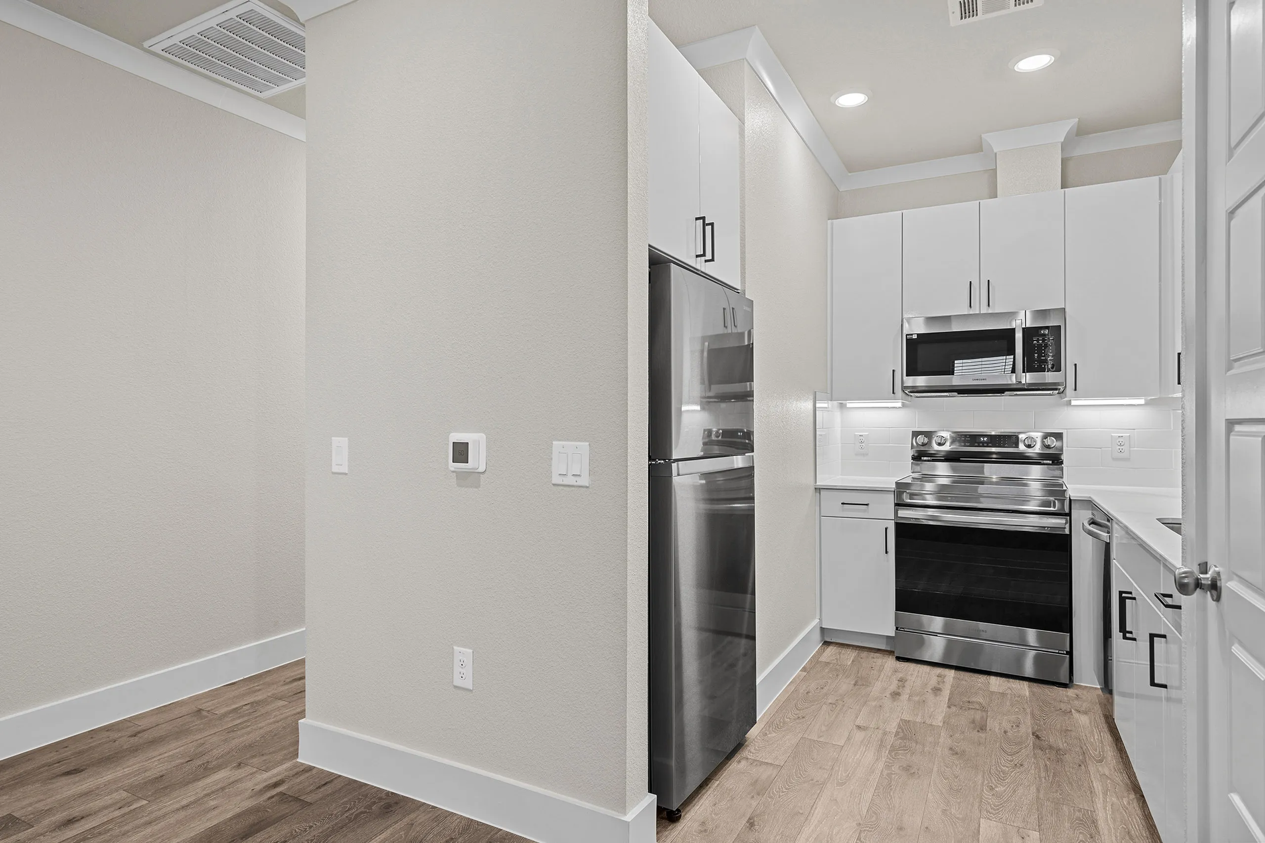 Modern kitchen with sleek stainless steel appliances, elegant white cabinetry, and warm wood flooring.