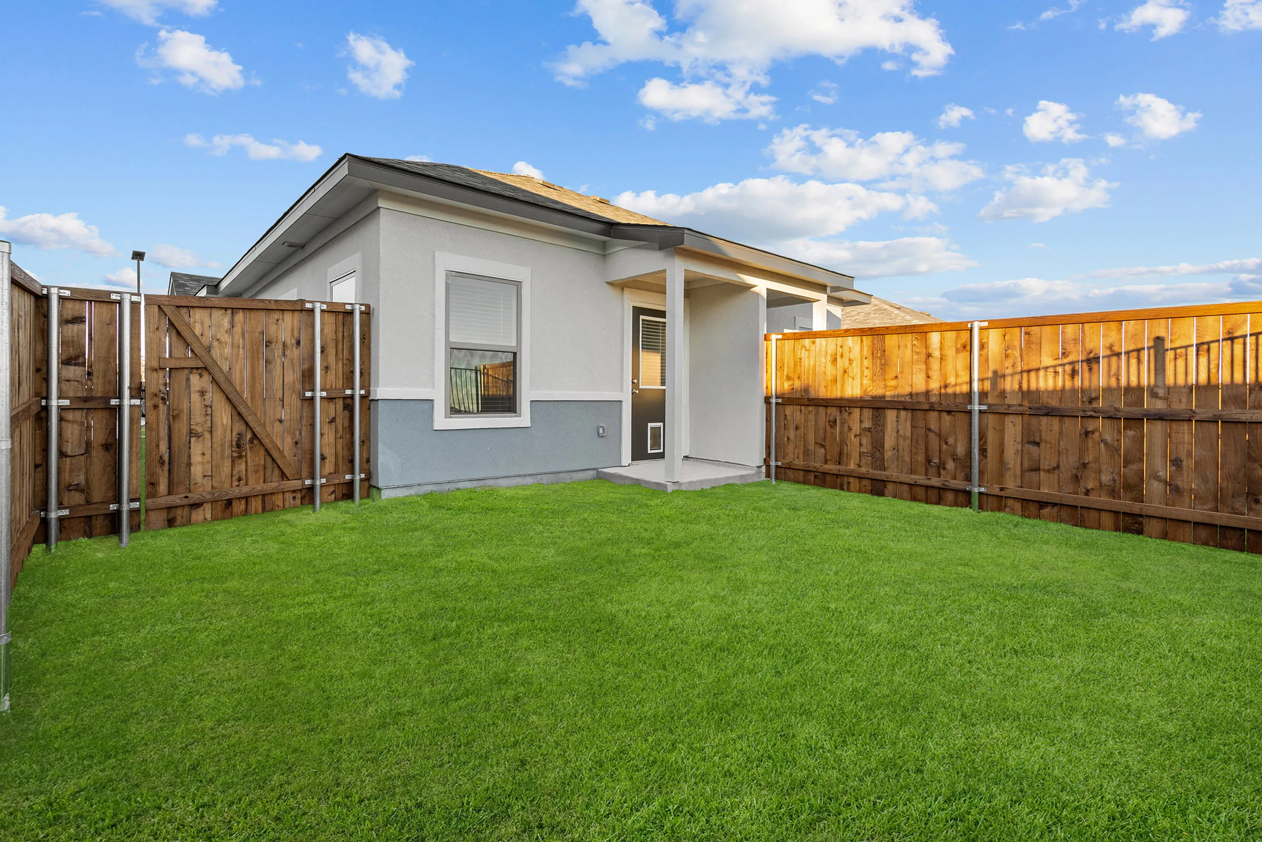 Charming home exterior with fenced backyard and lush green lawn, featuring a cozy patio and blue sky backdrop.