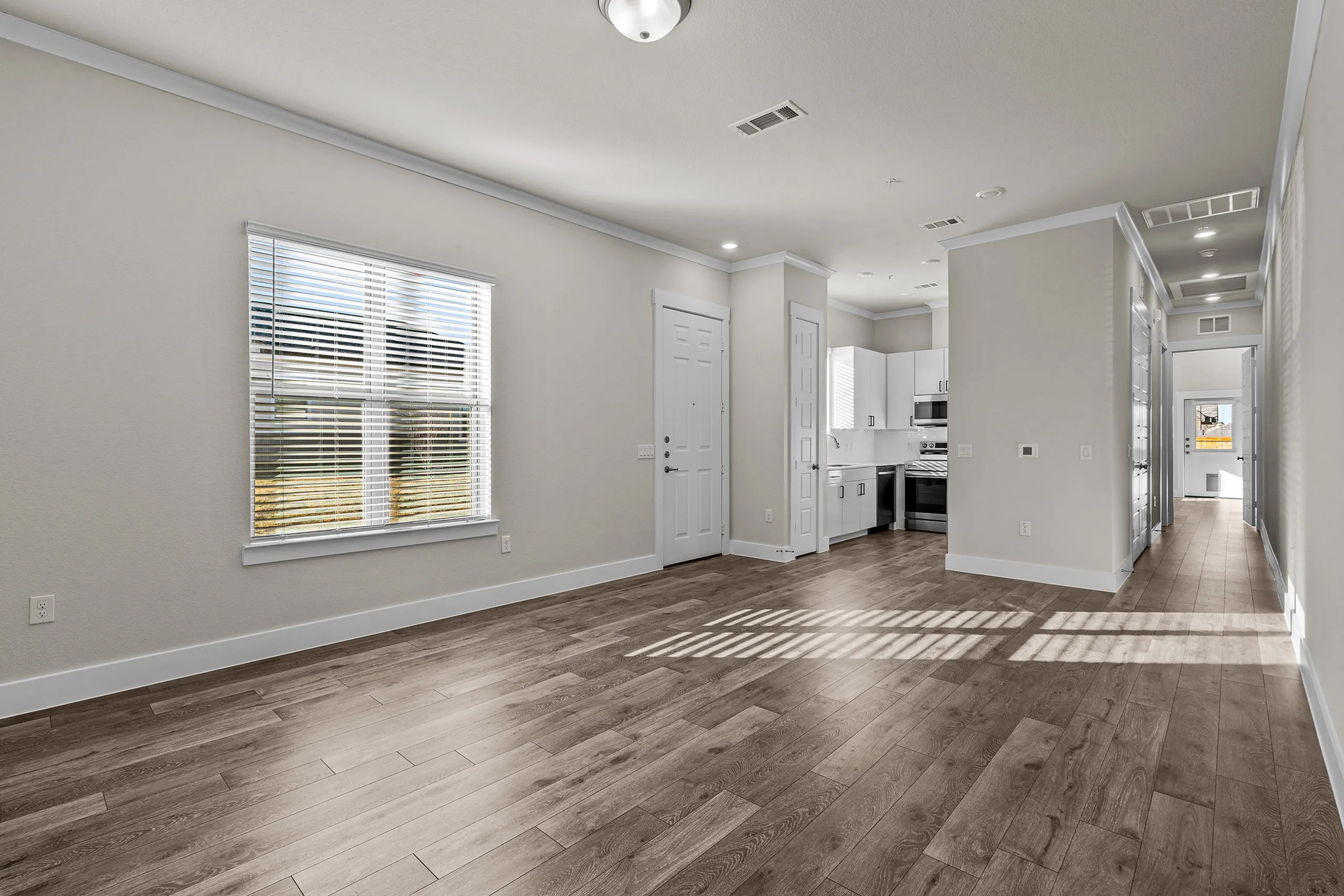 Bright and modern living area with sleek hardwood floors, pristine white walls, and a stylish open kitchen. Abundant natural light creates a warm and inviting atmosphere.