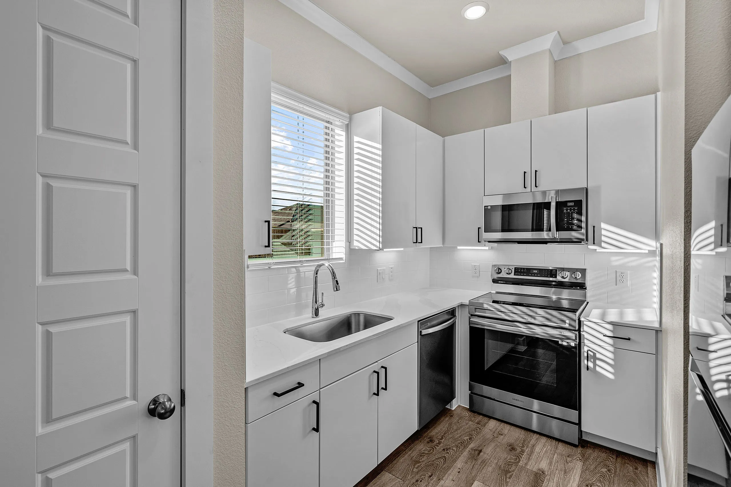 Modern kitchen with sleek white cabinetry, stainless steel appliances, and elegant hardwood flooring, bathed in natural light.