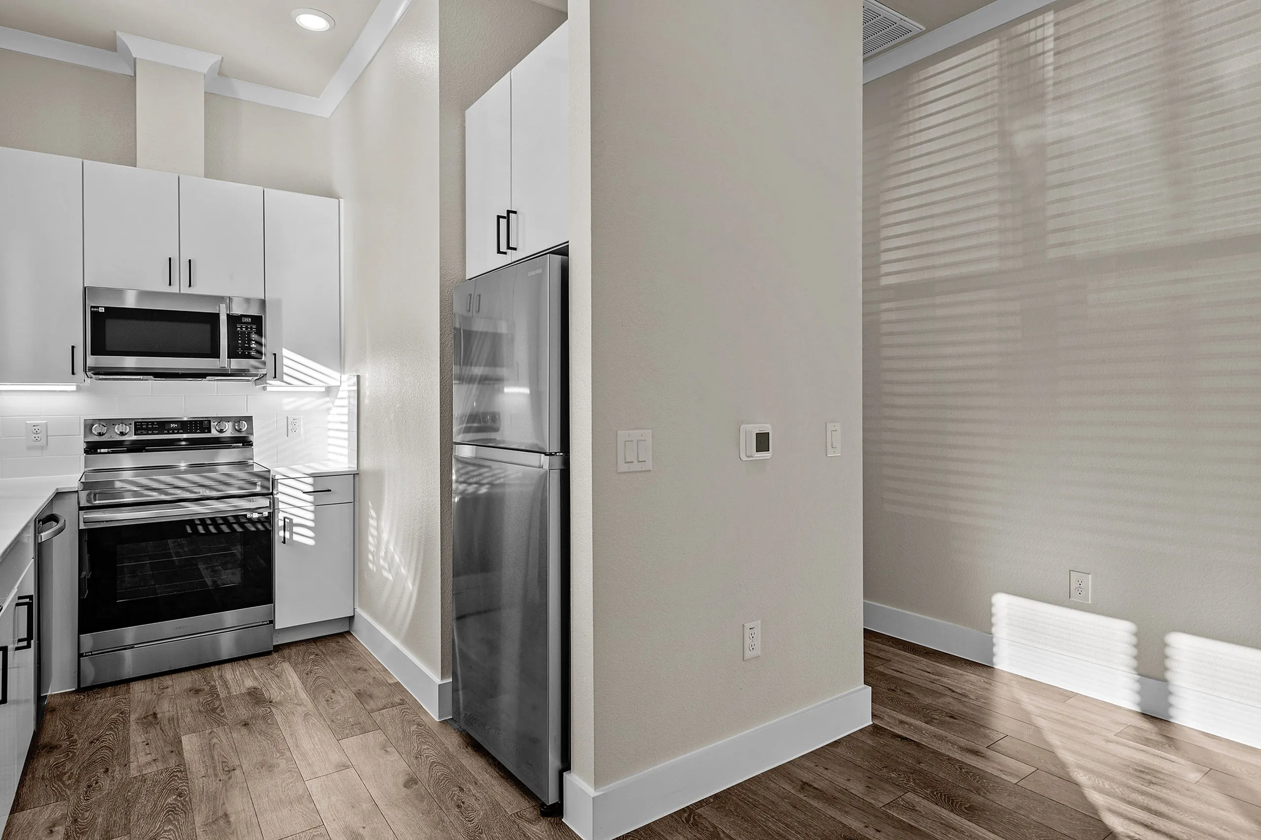 Modern kitchen with sleek stainless steel appliances, white cabinetry, and elegant wood flooring.