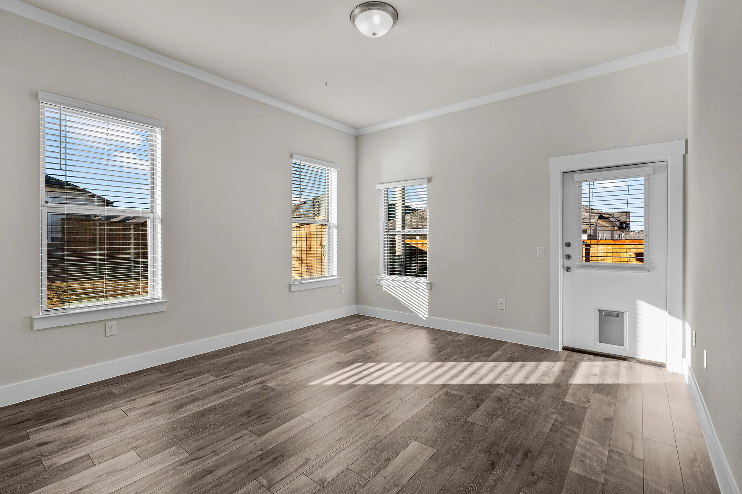 Bright and spacious room with elegant hardwood flooring, large windows, and a stylish door, perfect for a cozy living space.