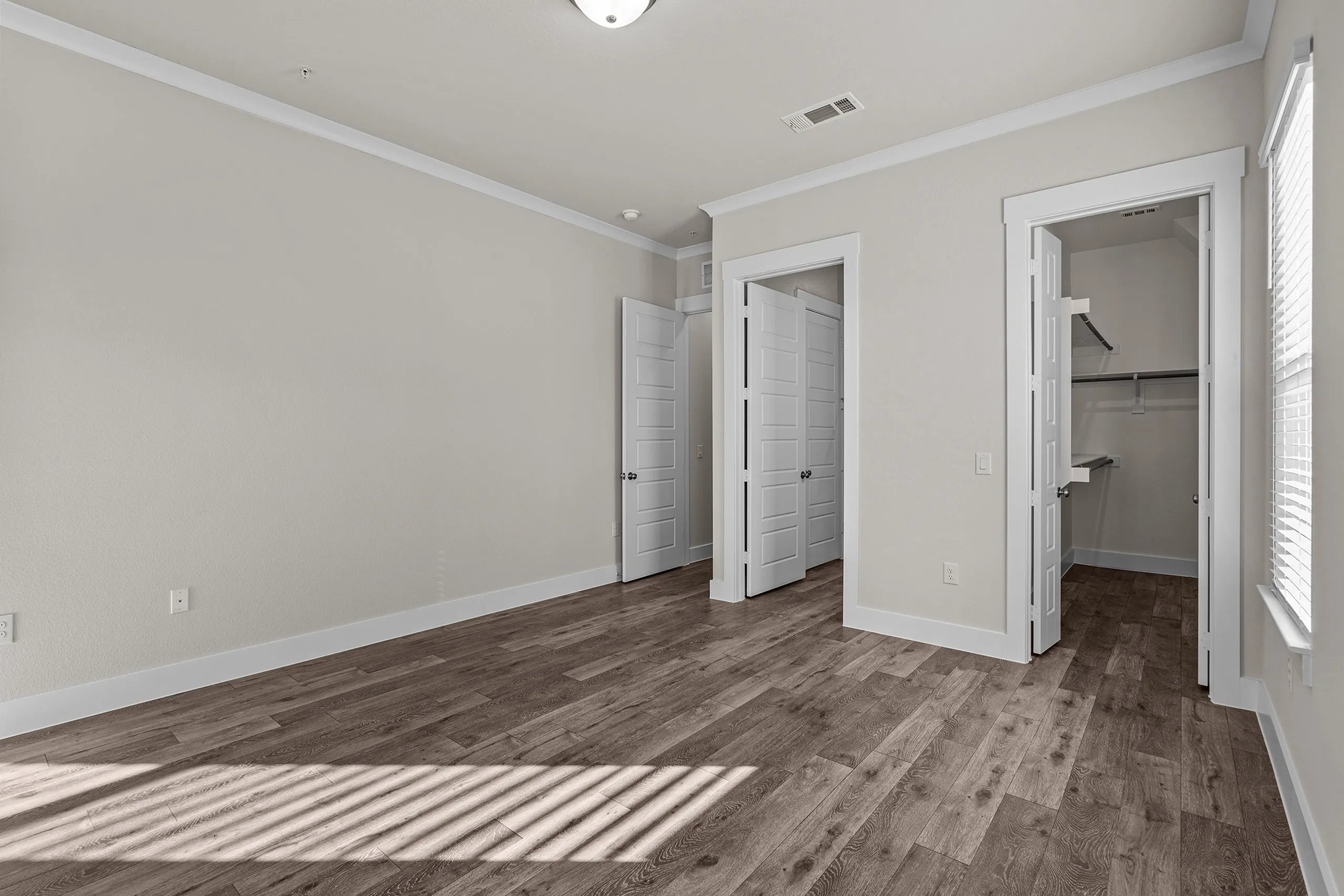 Elegant bedroom with ample natural light, featuring hardwood floors and spacious walk-in closet.