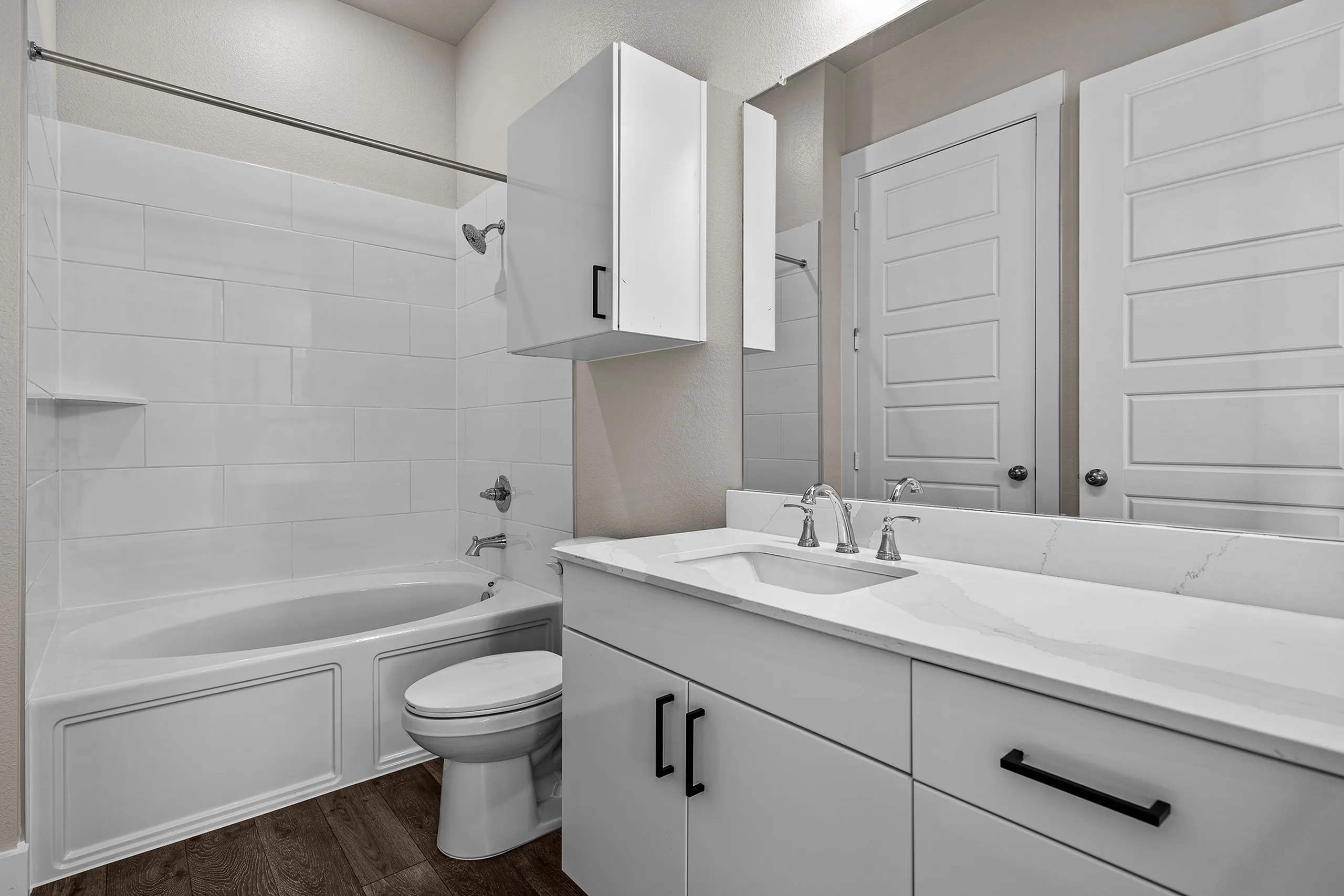 Modern bathroom with sleek white cabinetry, marble-style countertop, and elegant fixtures beside a pristine bathtub.