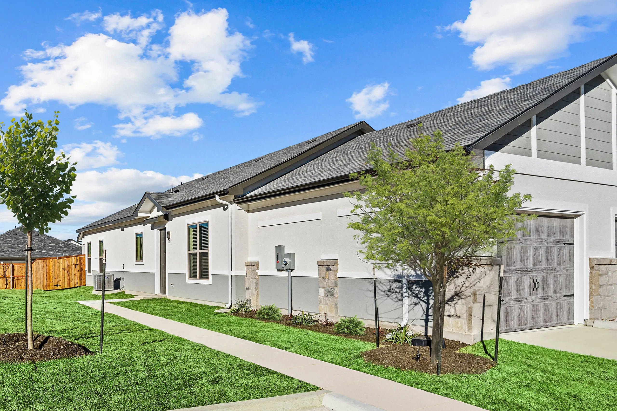 Charming modern house exterior with manicured lawn, vibrant greenery, and a sleek design under a bright blue sky.