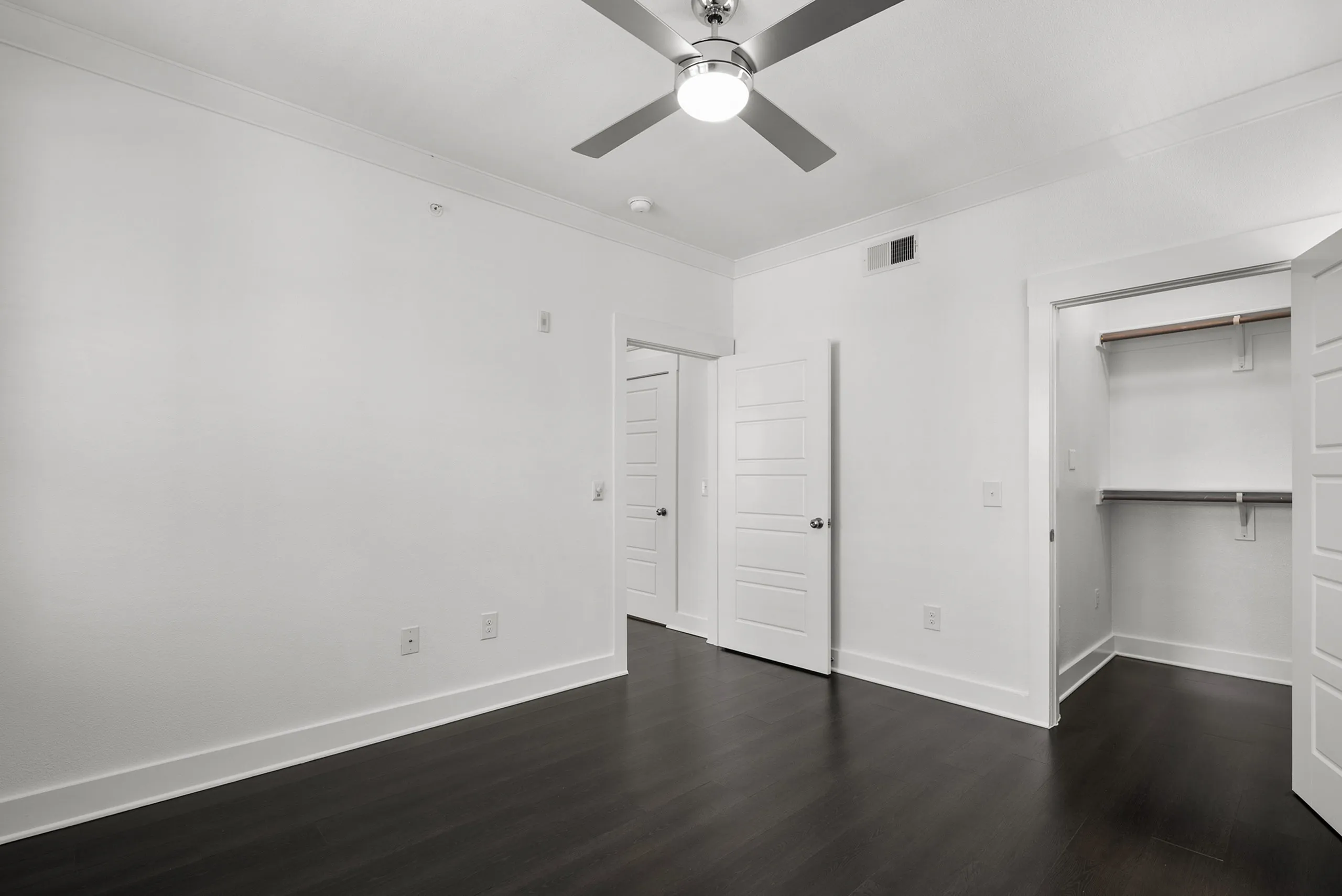 Bright, modern room with sleek dark hardwood floors, a stylish ceiling fan, and a spacious walk-in closet.