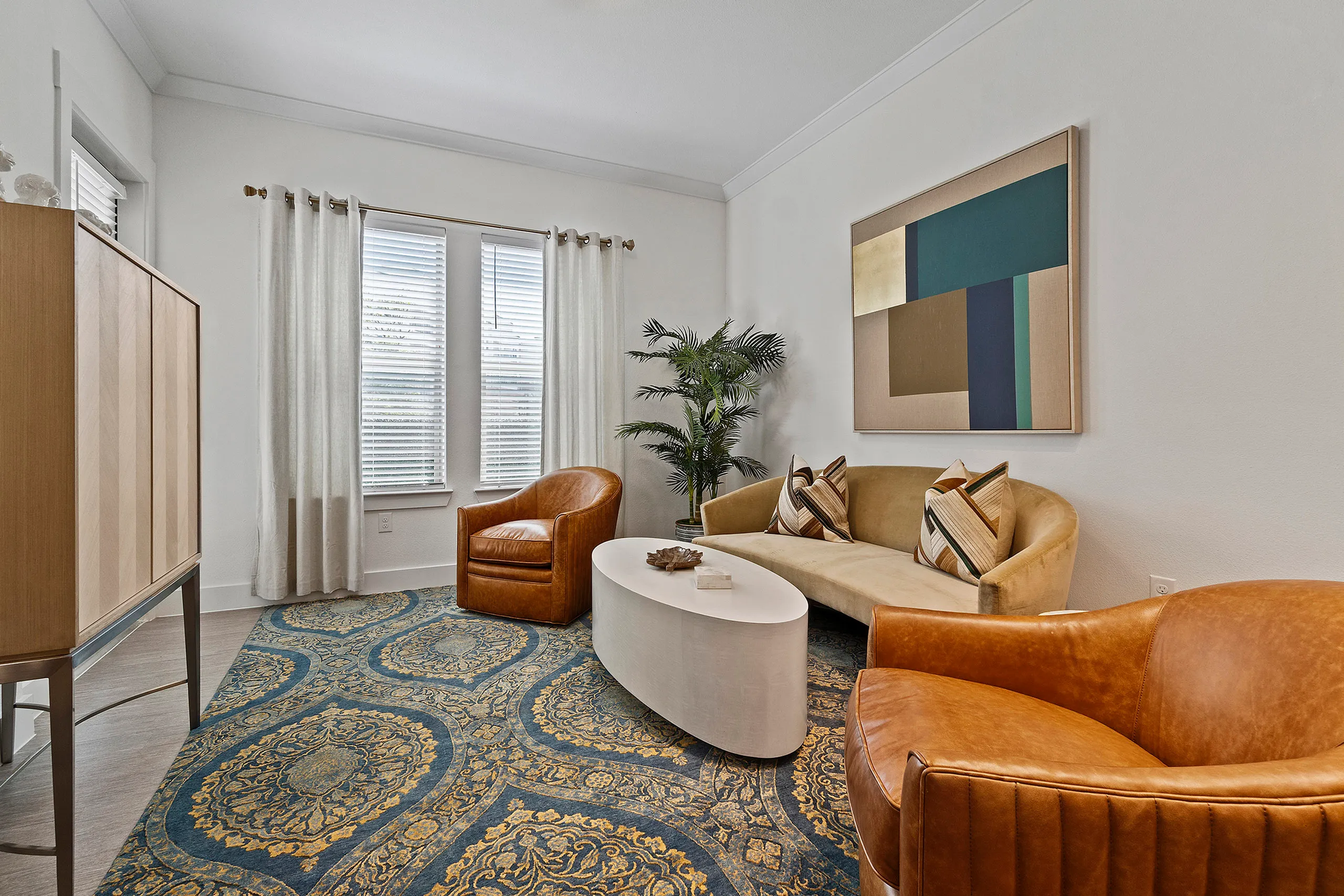 Cozy modern living room with a plush sofa, stylish armchairs, vibrant abstract artwork, and a lush plant for a welcoming ambiance.