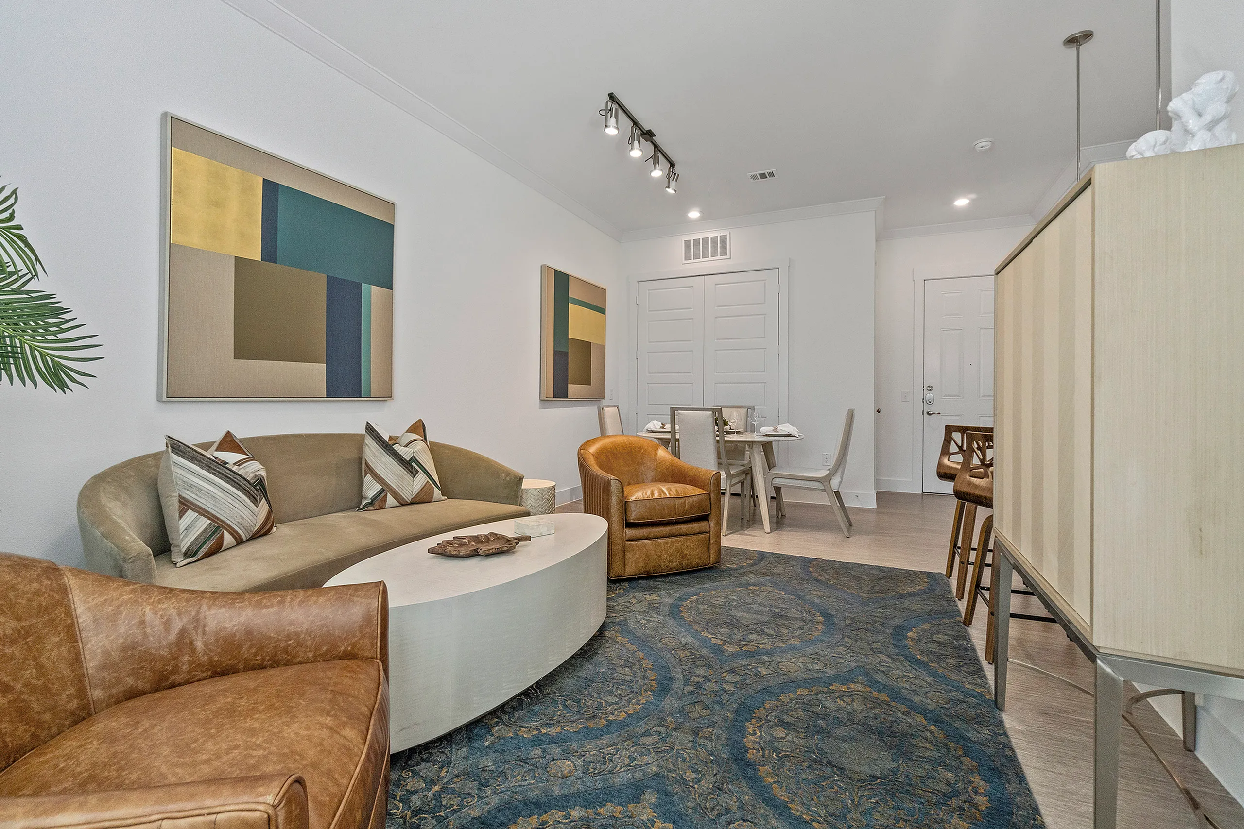 Elegant living room with modern art, cozy seating, and a dining area, featuring contemporary decor and warm lighting.