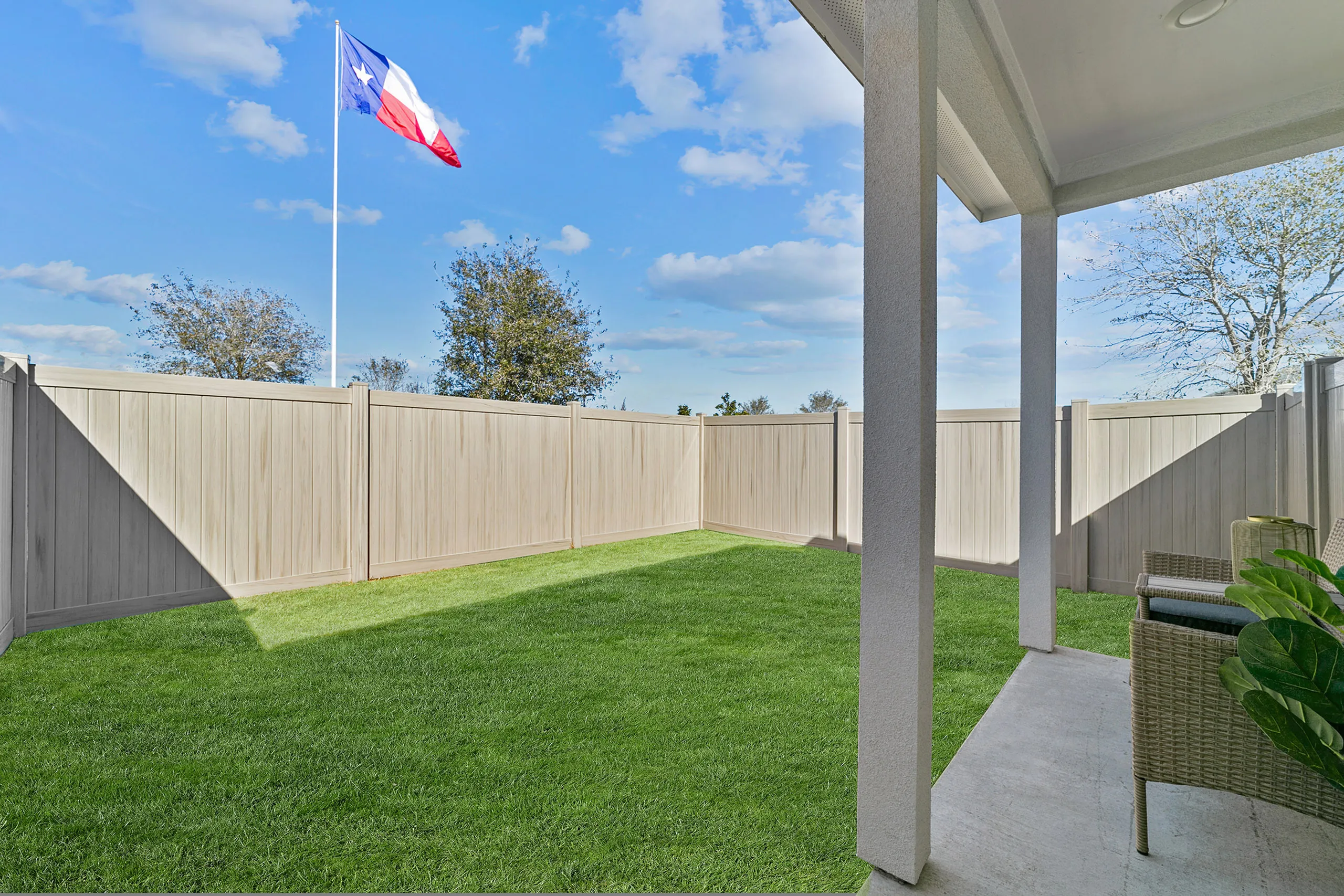 Inviting backyard view featuring a lush green lawn and cozy patio seating under a clear blue sky, with a Texas flag waving in the distance, ideal for relaxation and outdoor living.