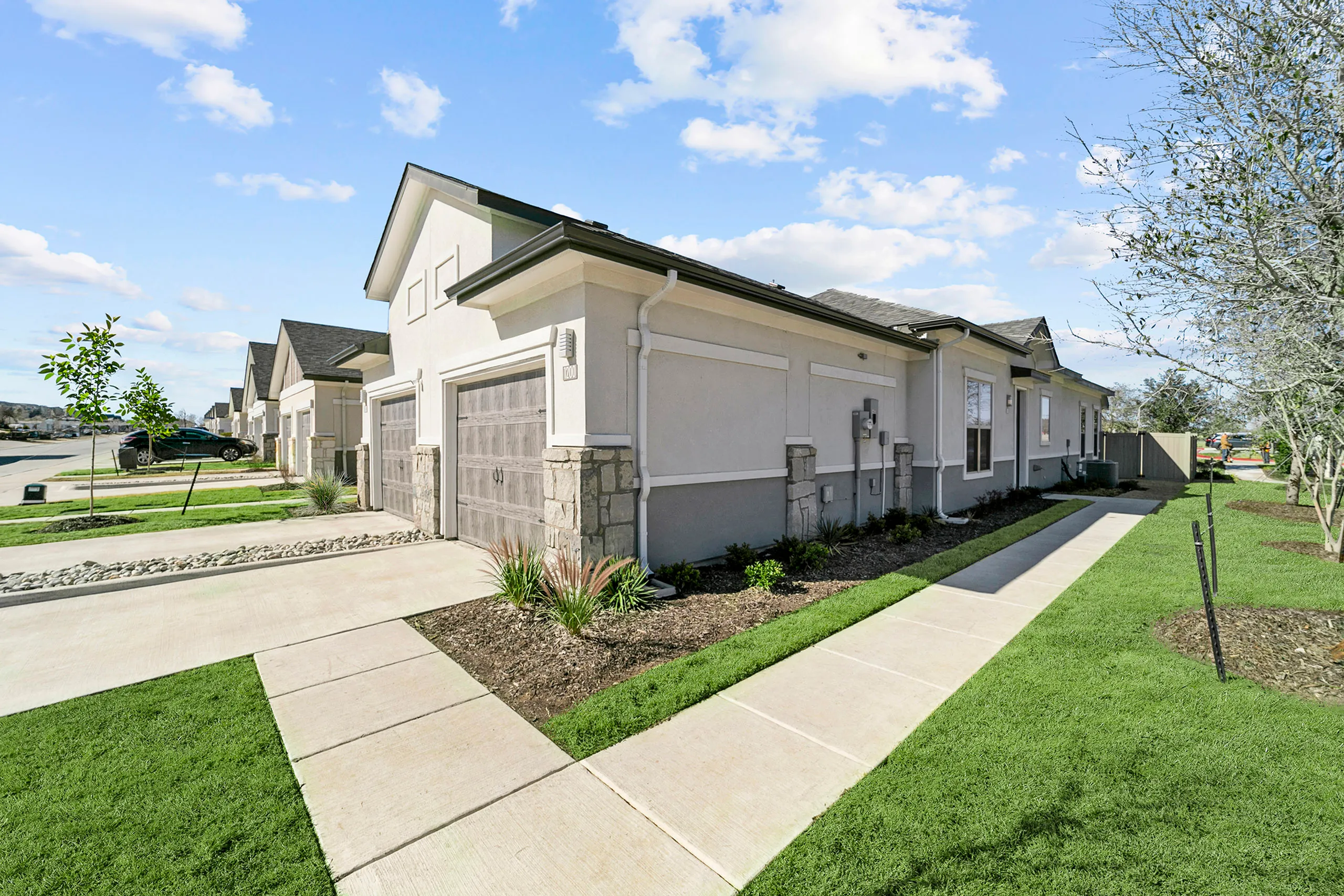 Modern residential complex with charming single-story homes, featuring sleek stone accents and well-maintained landscaping on a sunny day.