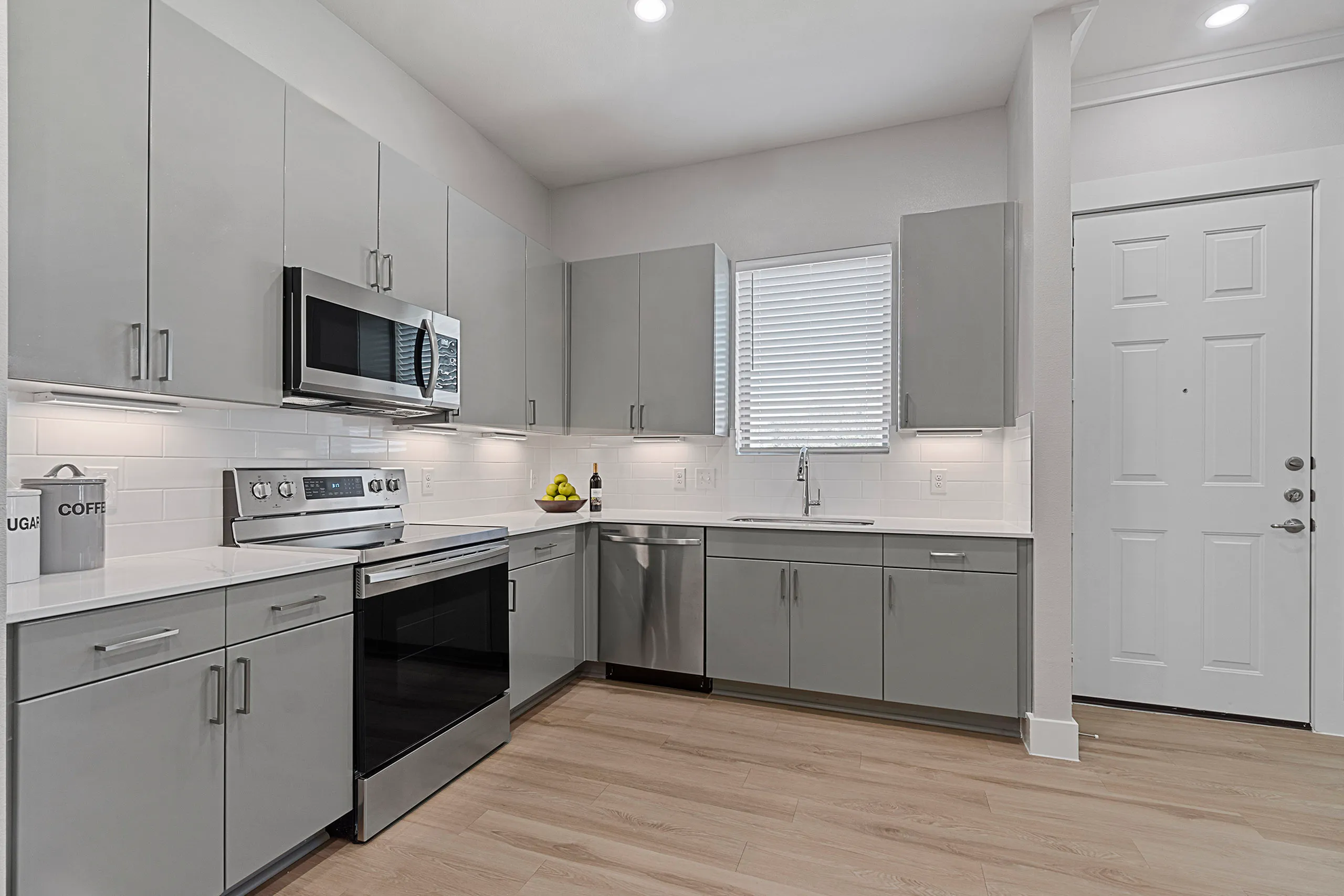 Modern kitchen with sleek gray cabinetry, stainless steel appliances, and bright overhead lighting. Spacious design with ample countertop space.