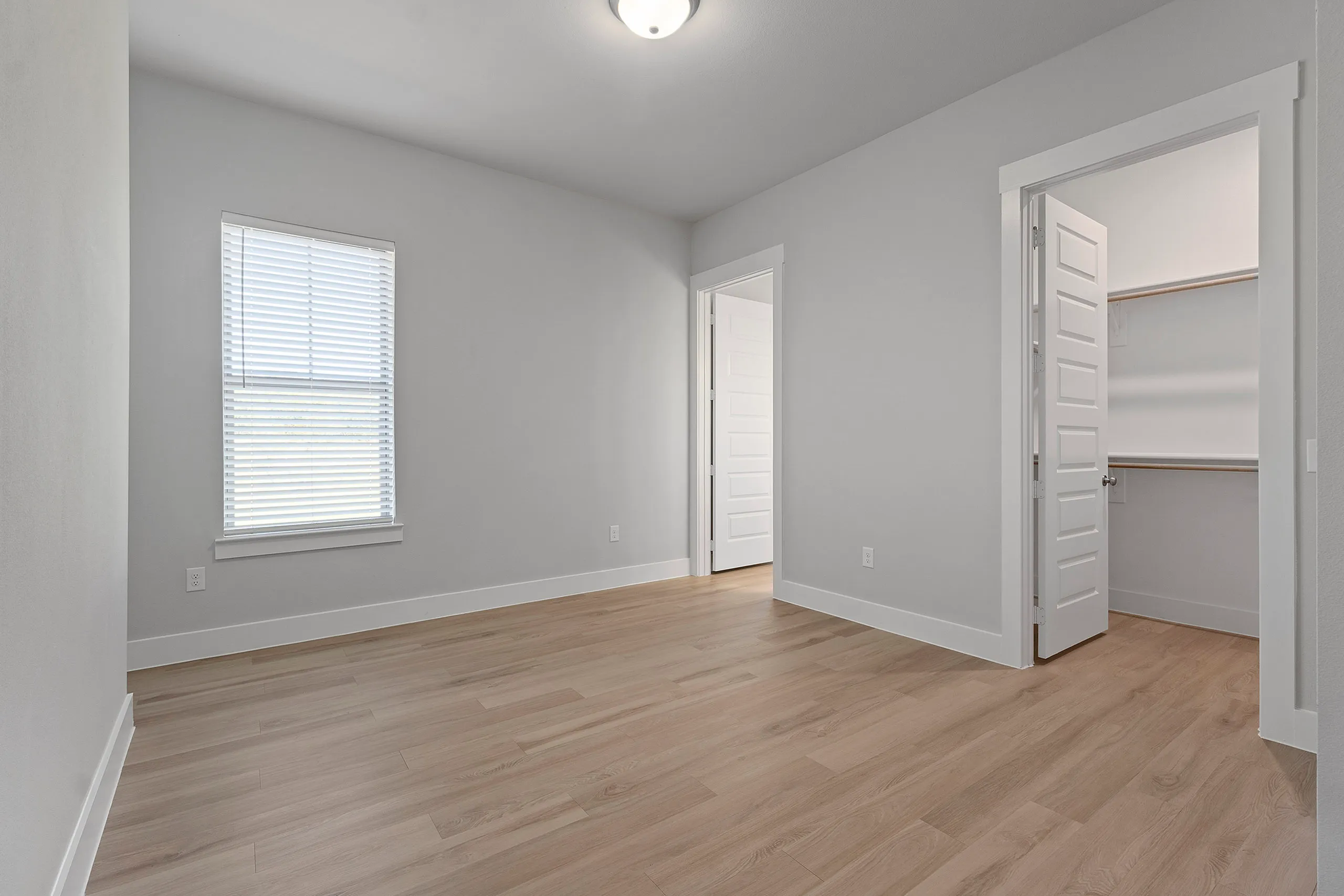 Bright and airy empty room with natural light, hardwood flooring, and a spacious walk-in closet.