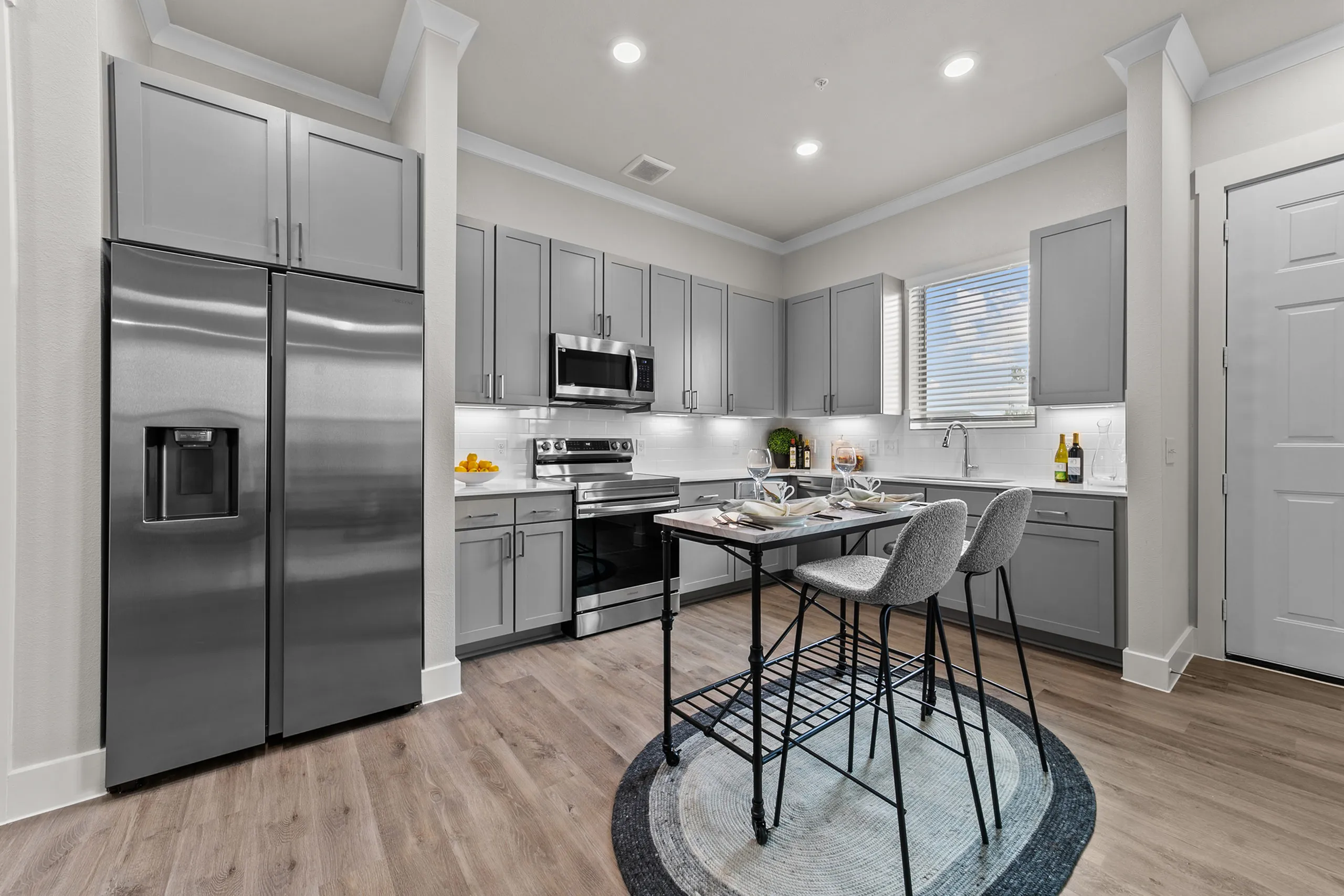 Modern kitchen with sleek gray cabinetry, stainless steel appliances, and elegant dining setup on a stylish rug.