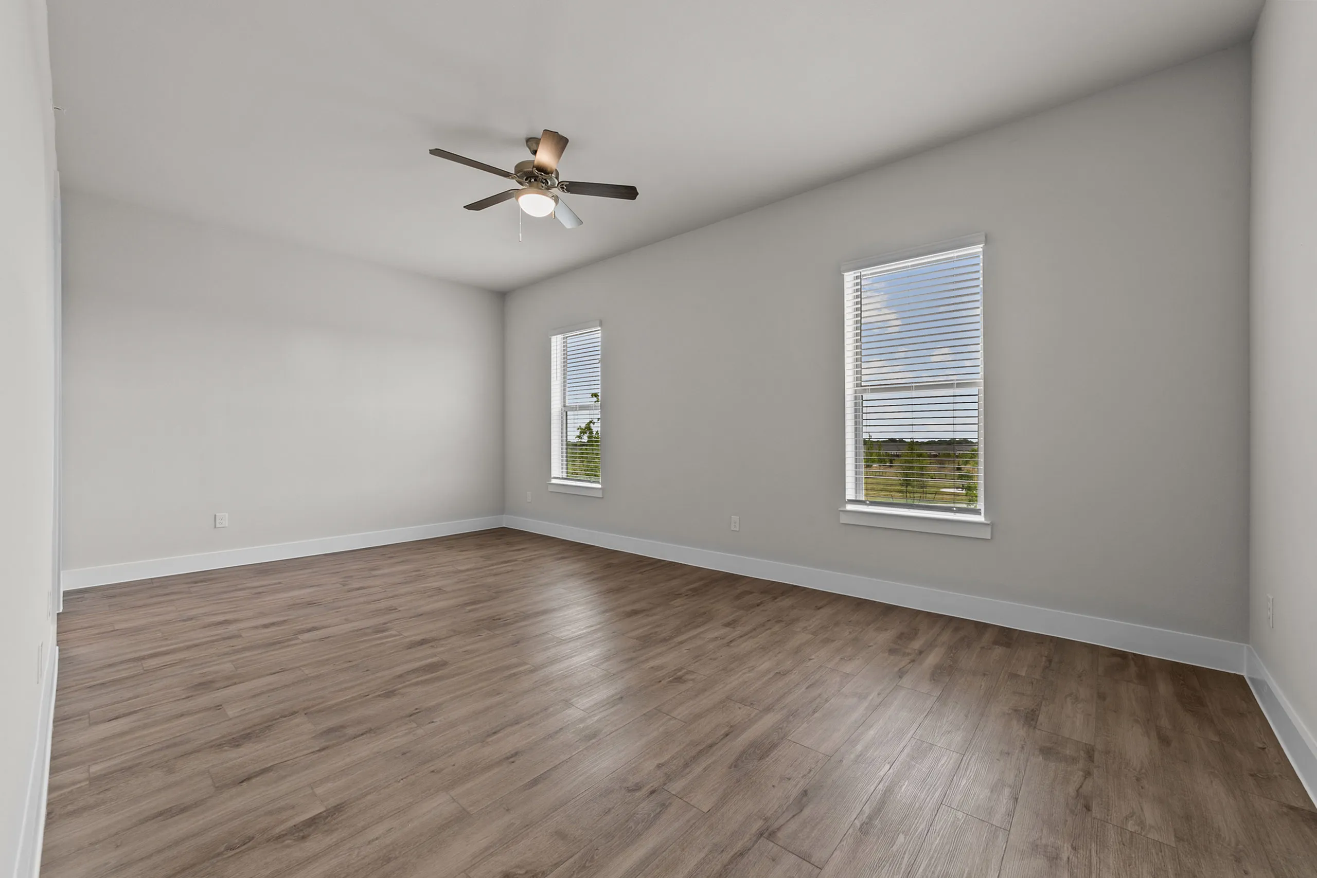 Bright and spacious empty room with elegant wood flooring, large windows, and a modern ceiling fan.