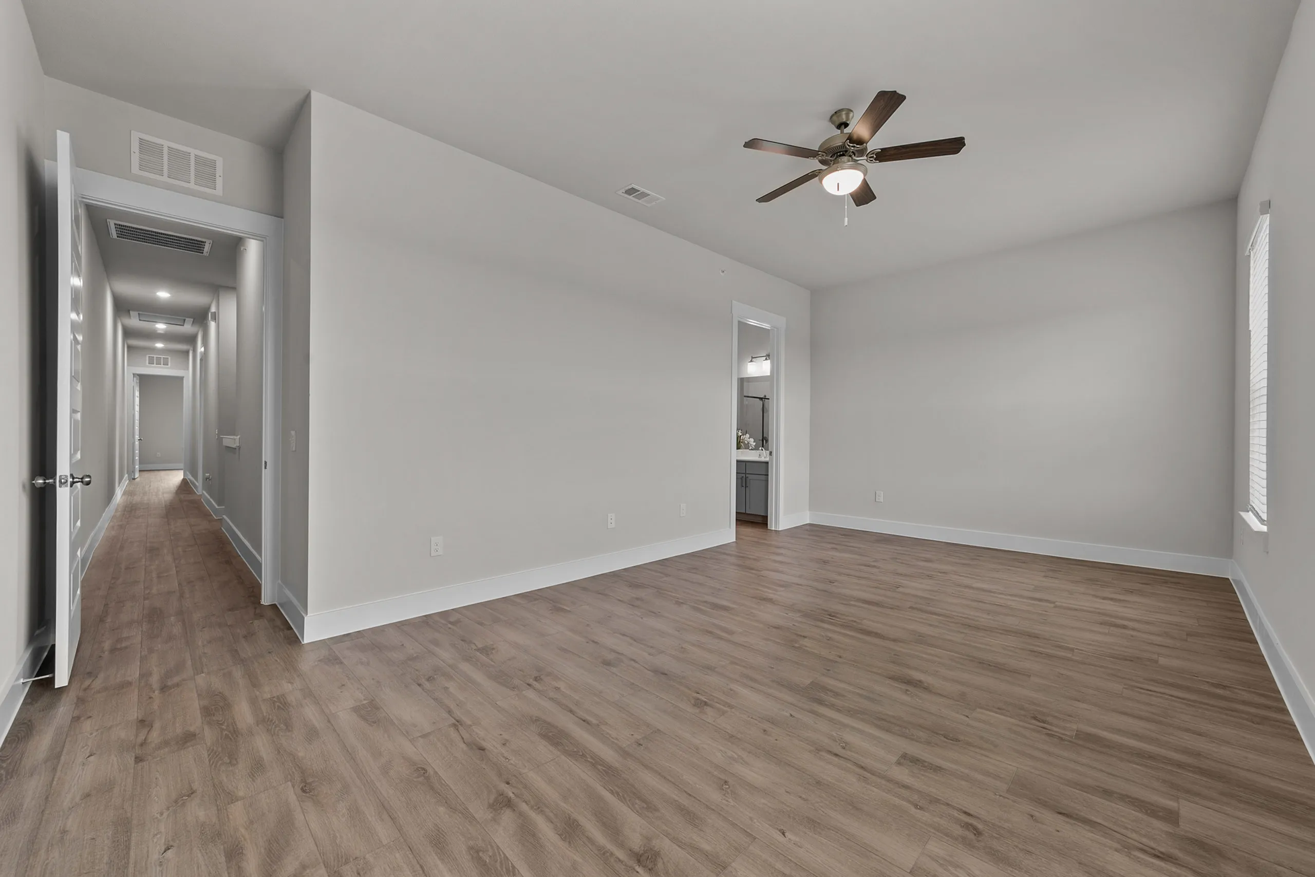 Spacious and modern apartment with elegant wood flooring, neutral walls, and stylish ceiling fan, leading to a bright hallway.