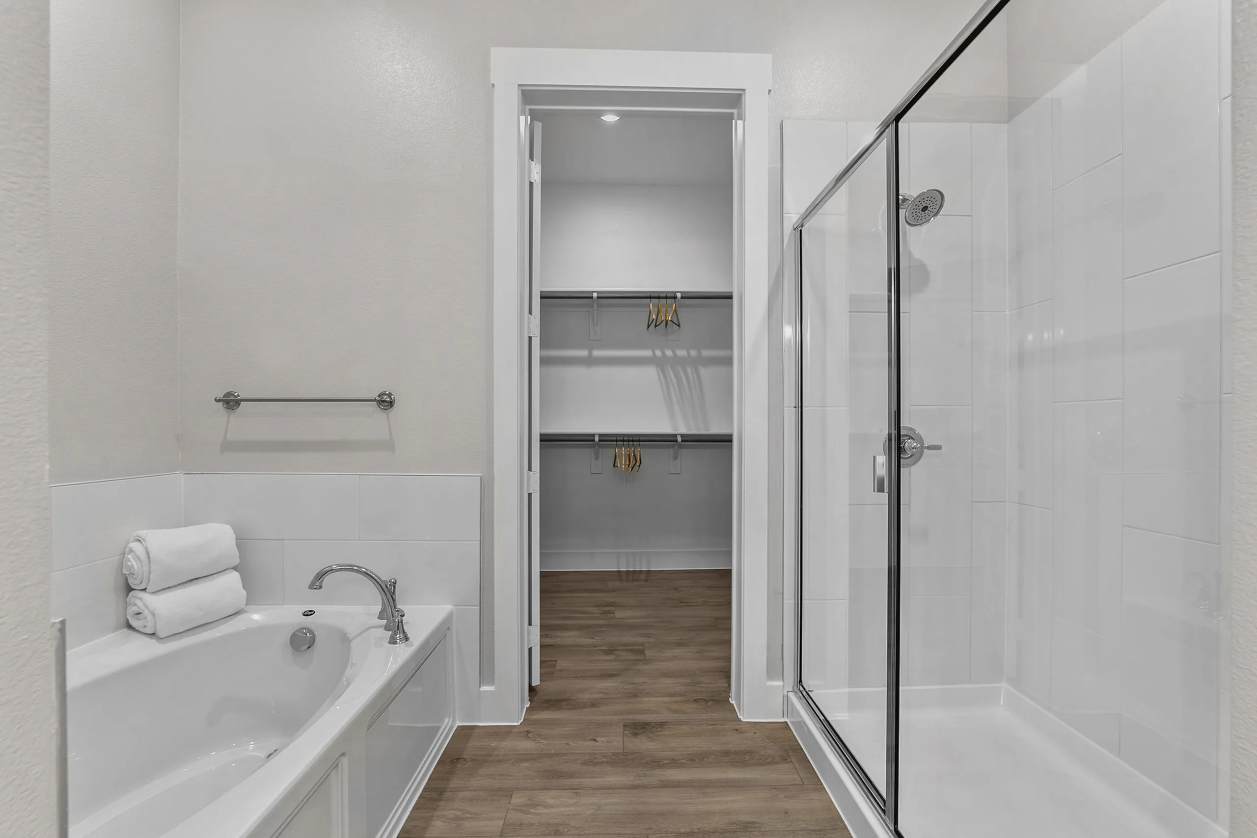 Modern bathroom featuring a sleek glass shower, luxurious soaking tub, and spacious walk-in closet with wooden flooring.