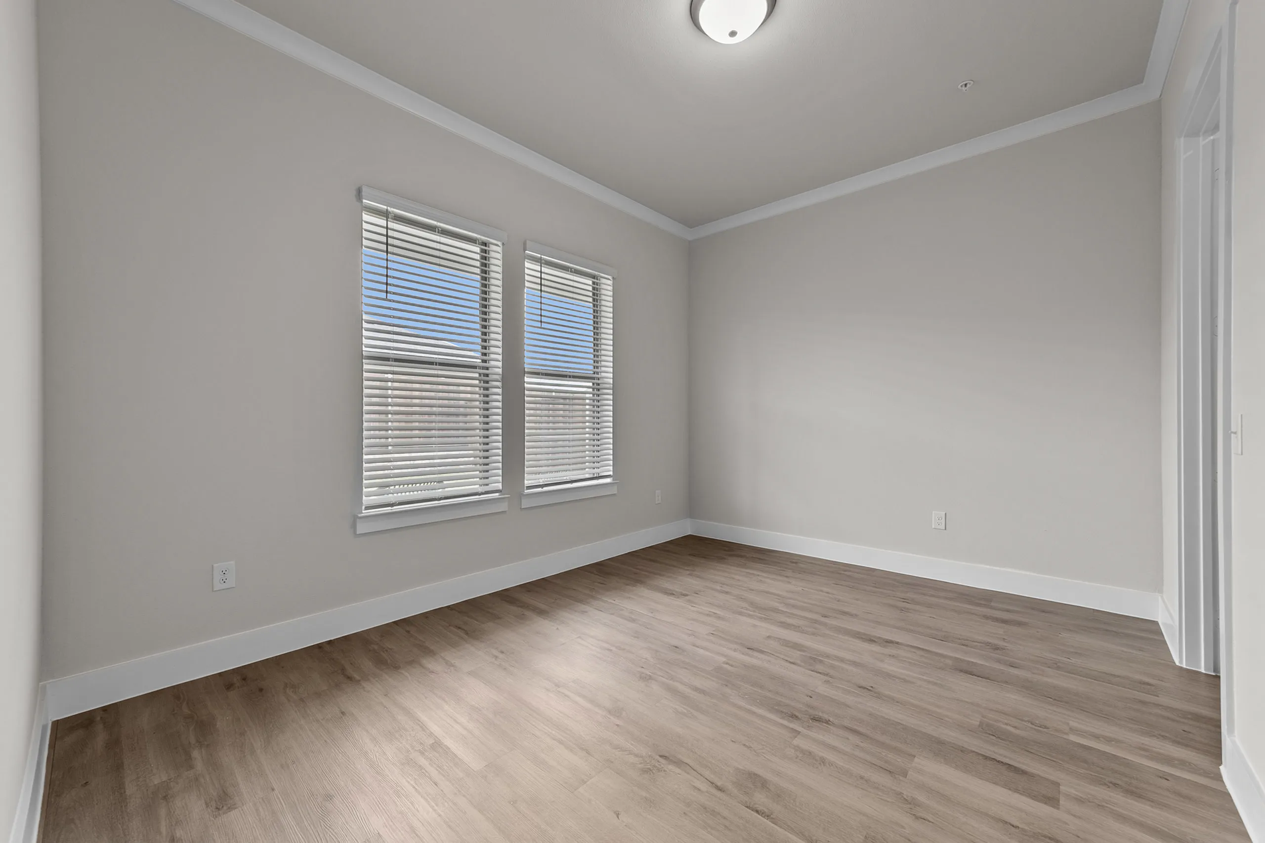 Bright and spacious bedroom with large windows, elegant wood flooring, and modern white walls.