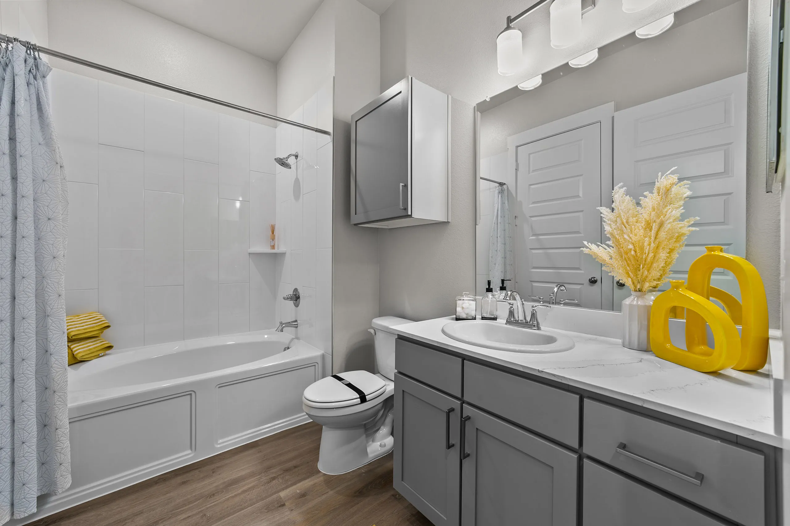 Modern bathroom design featuring a sleek gray vanity with a marble countertop, stylish lighting, and a bathtub with a shower. Complemented by bright yellow decor and elegant accessories.