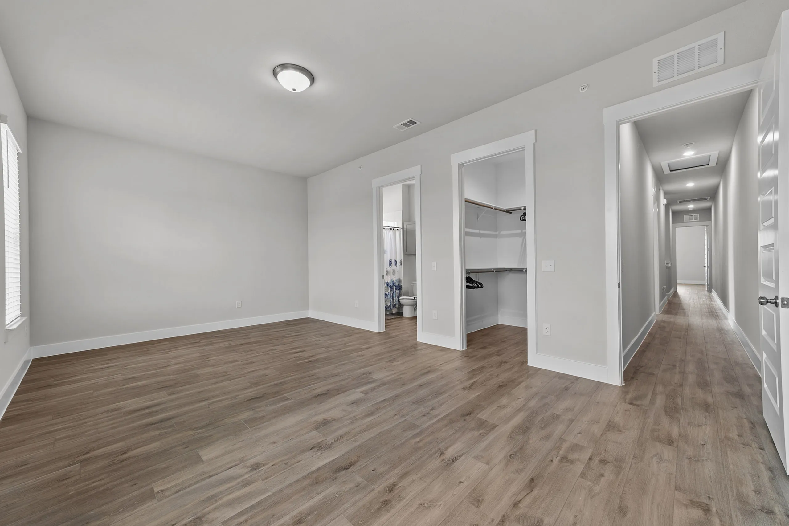 Spacious bedroom with elegant wood flooring, featuring a walk-in closet and modern en-suite bathroom. Natural light floods through large windows, creating an inviting atmosphere.