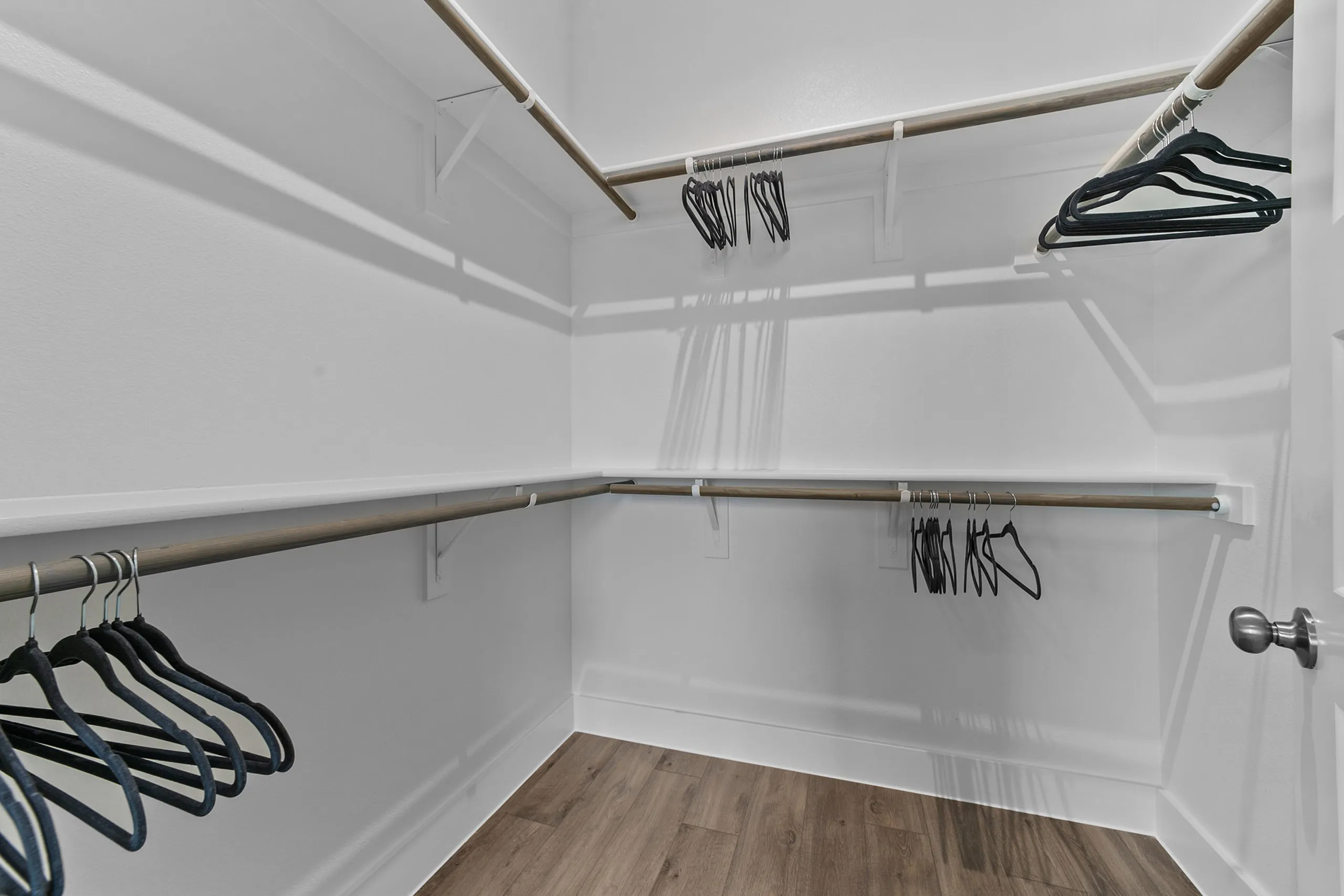 Spacious walk-in closet with elegant wooden flooring, equipped with multiple hanging rods and sleek black hangers.