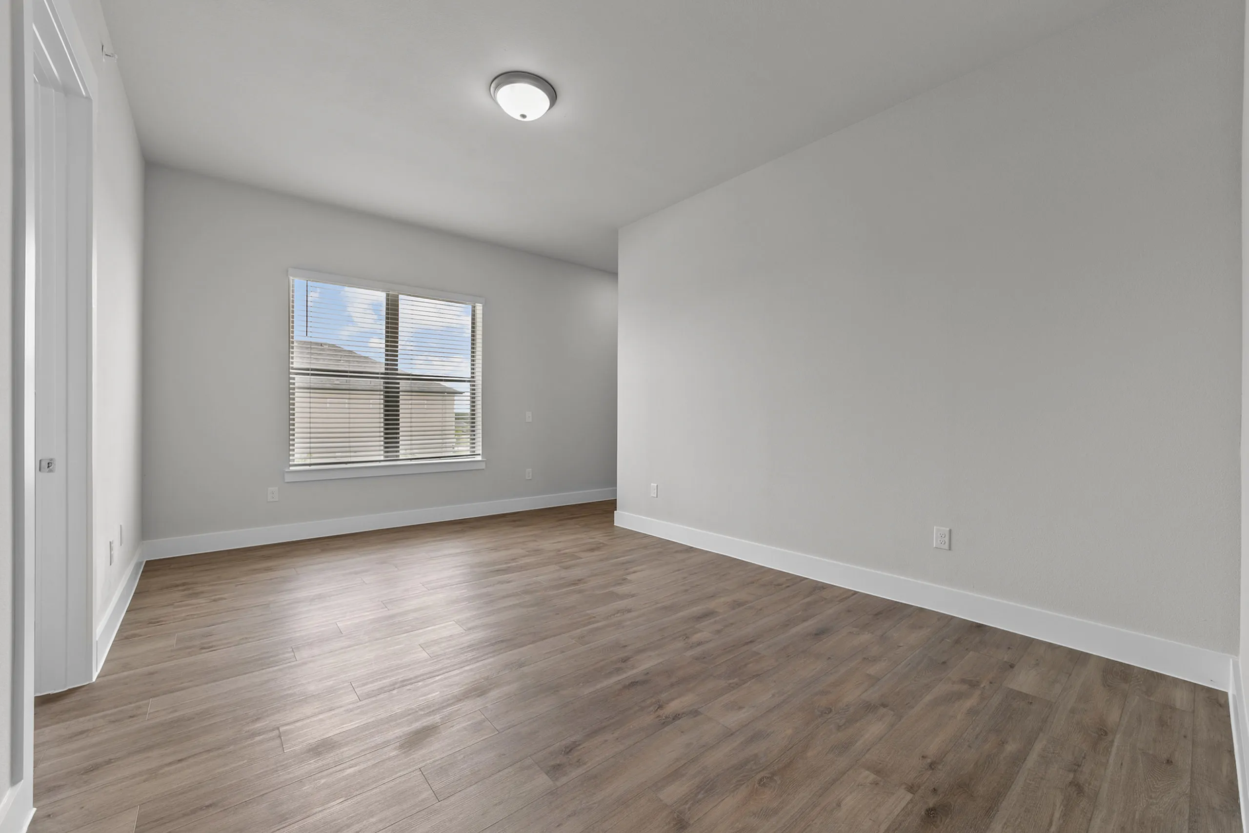 Bright, spacious room with elegant wood flooring and a large window offering ample natural light.