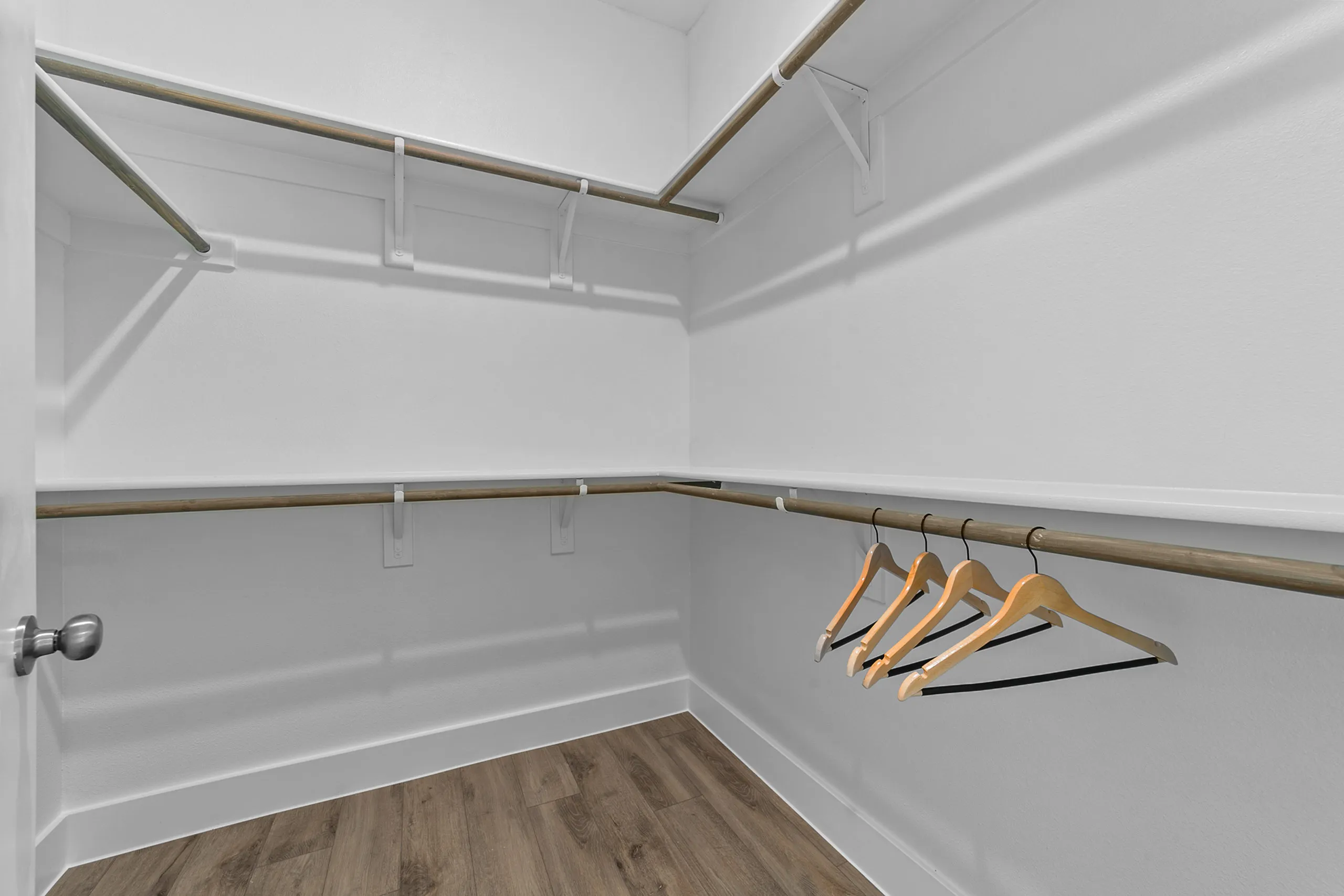 Spacious walk-in closet with sleek wooden flooring and ample hanging space.