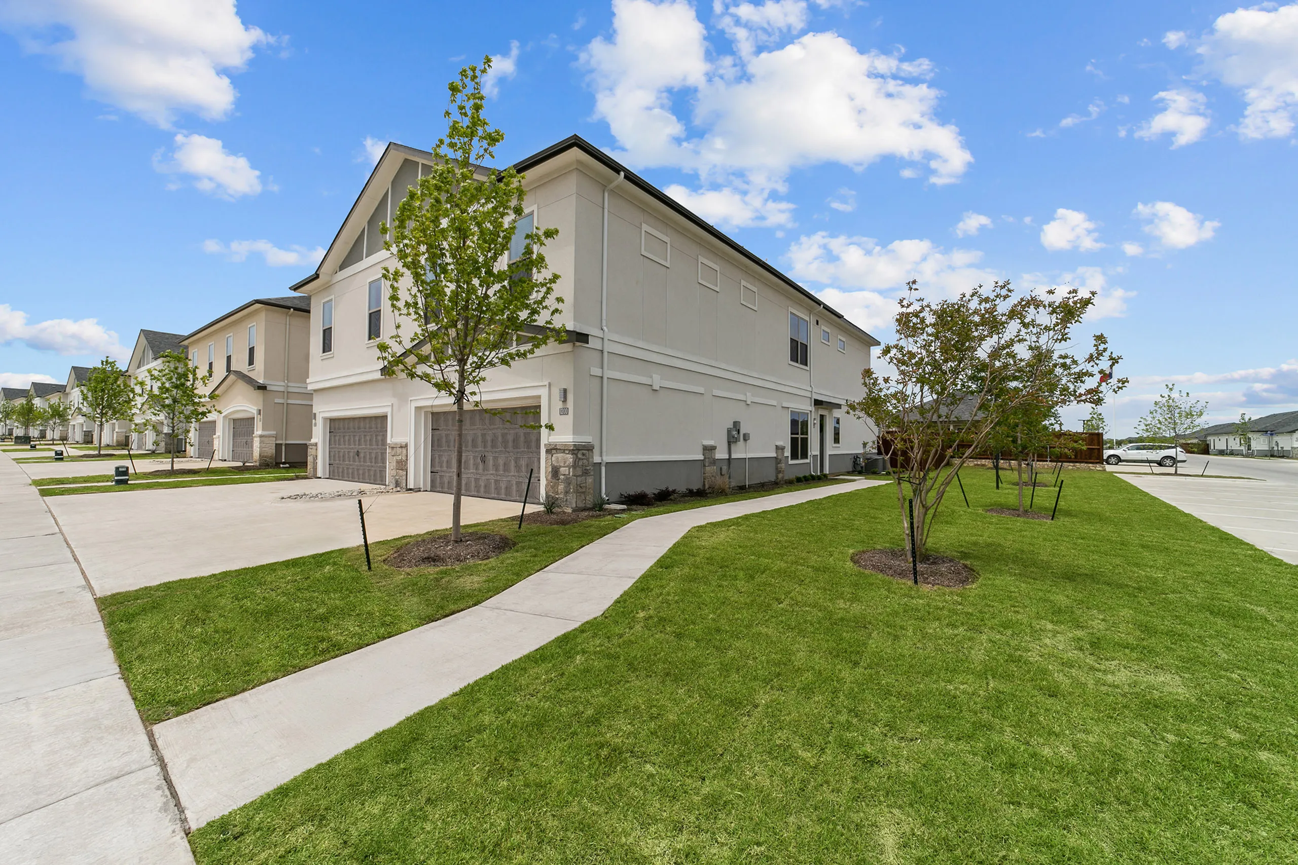 Charming residential street view showcasing modern townhouses with well-maintained lawns and vibrant landscaping under a sunny blue sky.