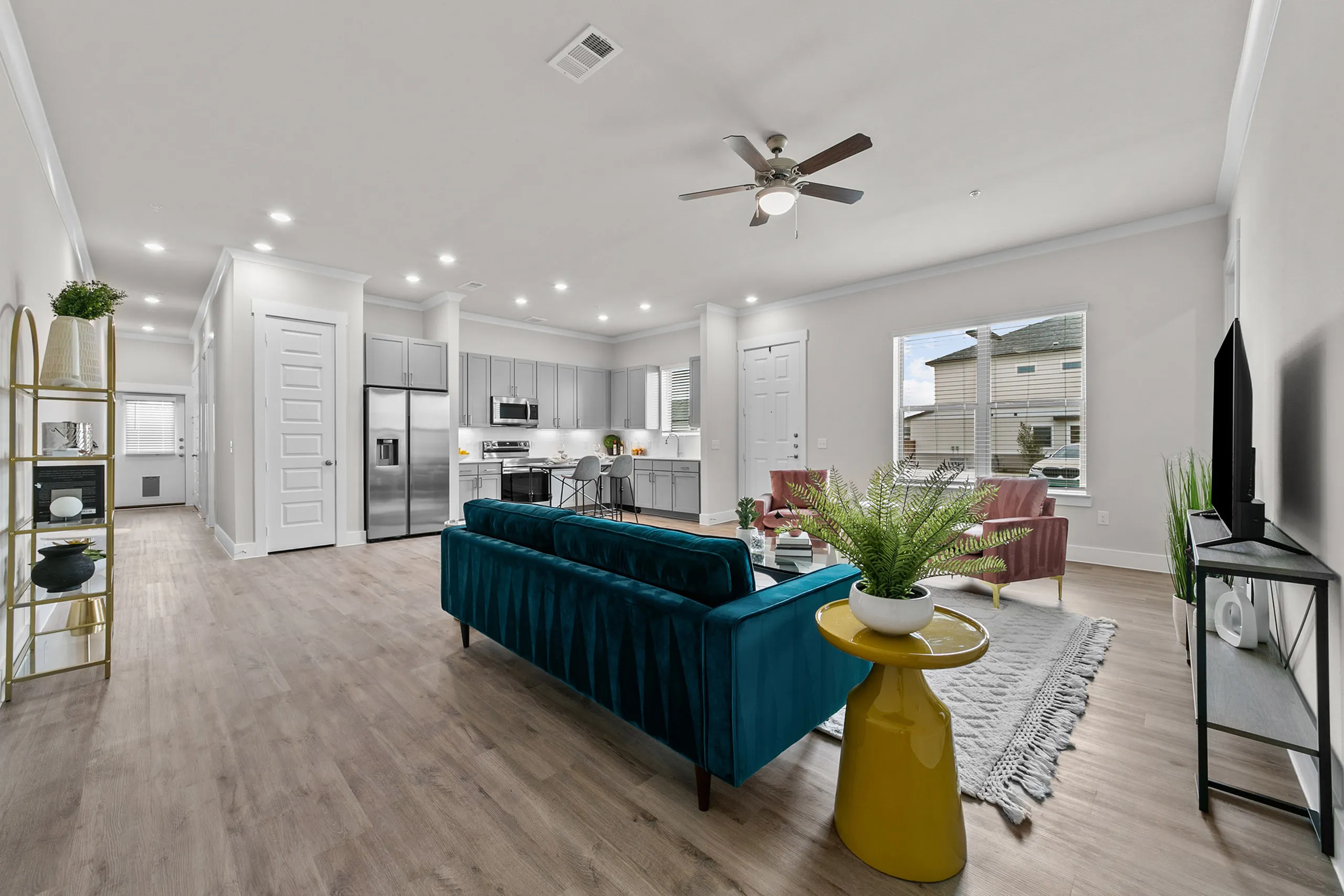 Modern open-concept living area featuring a sleek kitchen, stylish teal sofa, vibrant yellow side table, and elegant decor.