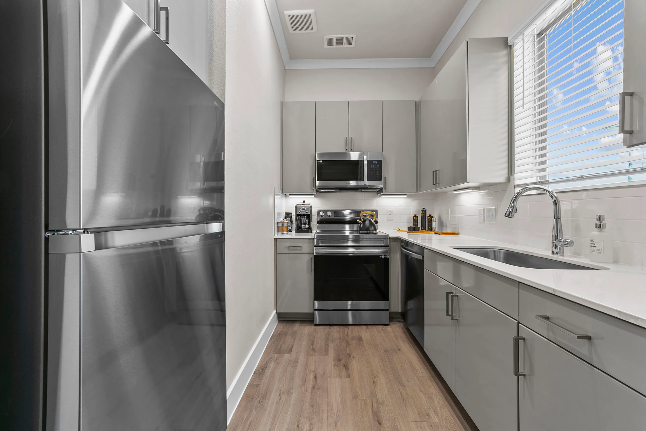 Modern kitchen featuring sleek stainless steel appliances, elegant grey cabinetry, and abundant natural light streaming through a large window.