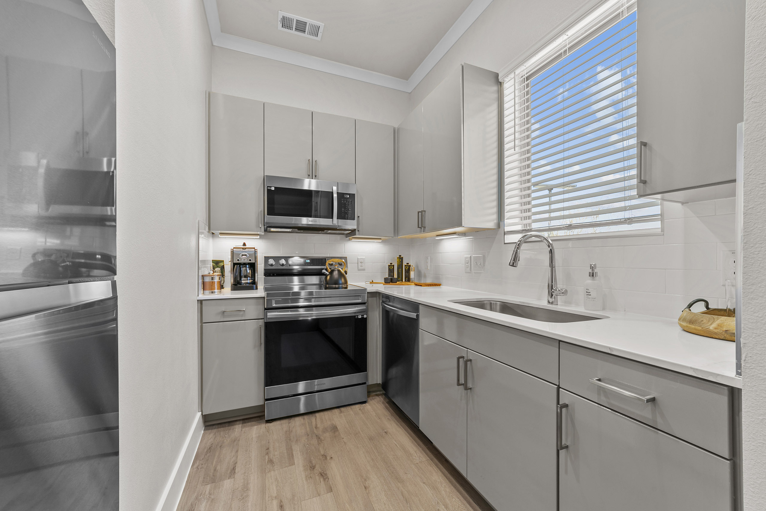Modern kitchen with sleek stainless steel appliances, light gray cabinets, and large window providing natural light.