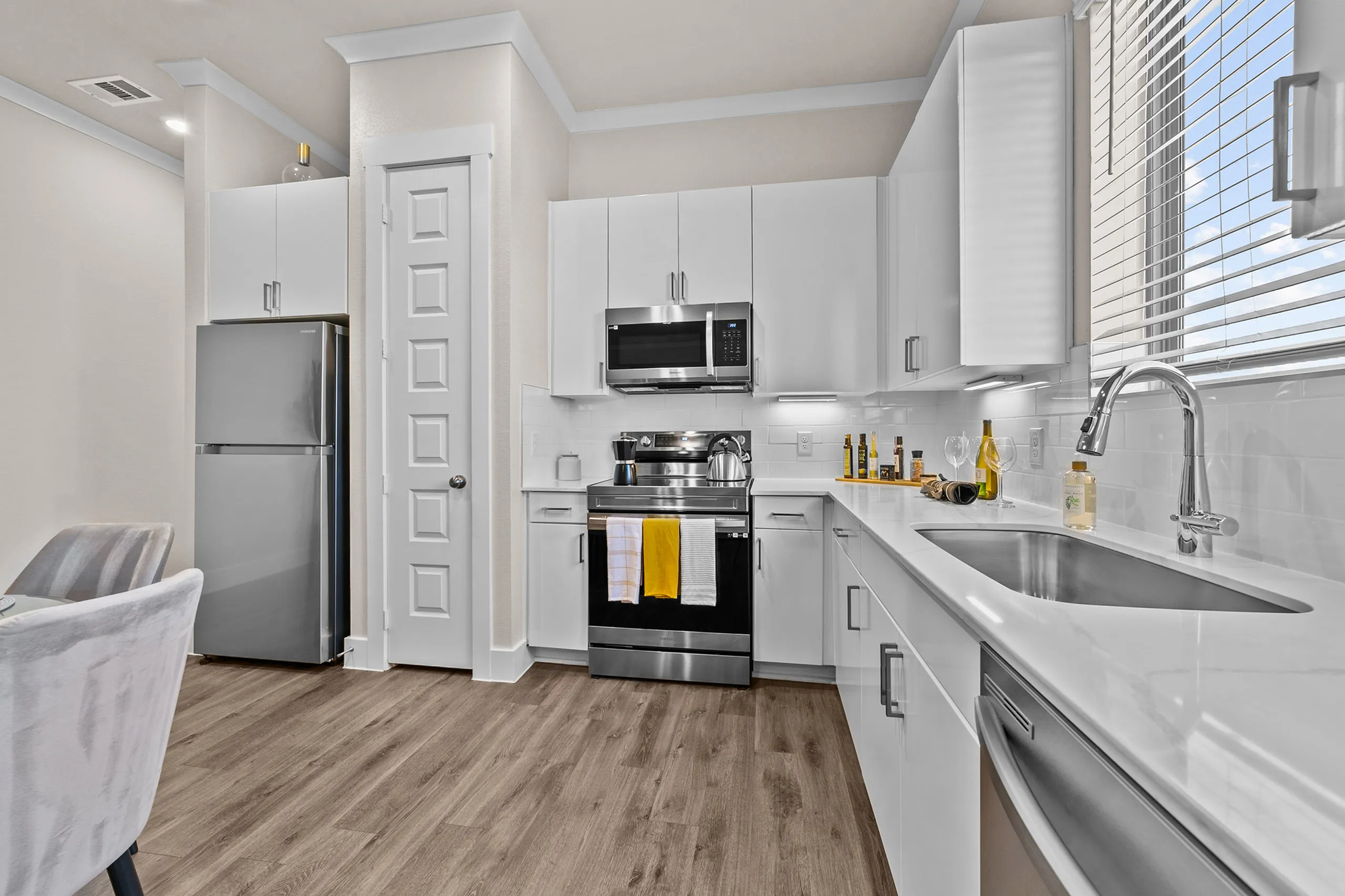 Modern kitchen with sleek white cabinetry, stainless steel appliances, and elegant wood flooring, offering a bright and airy atmosphere.