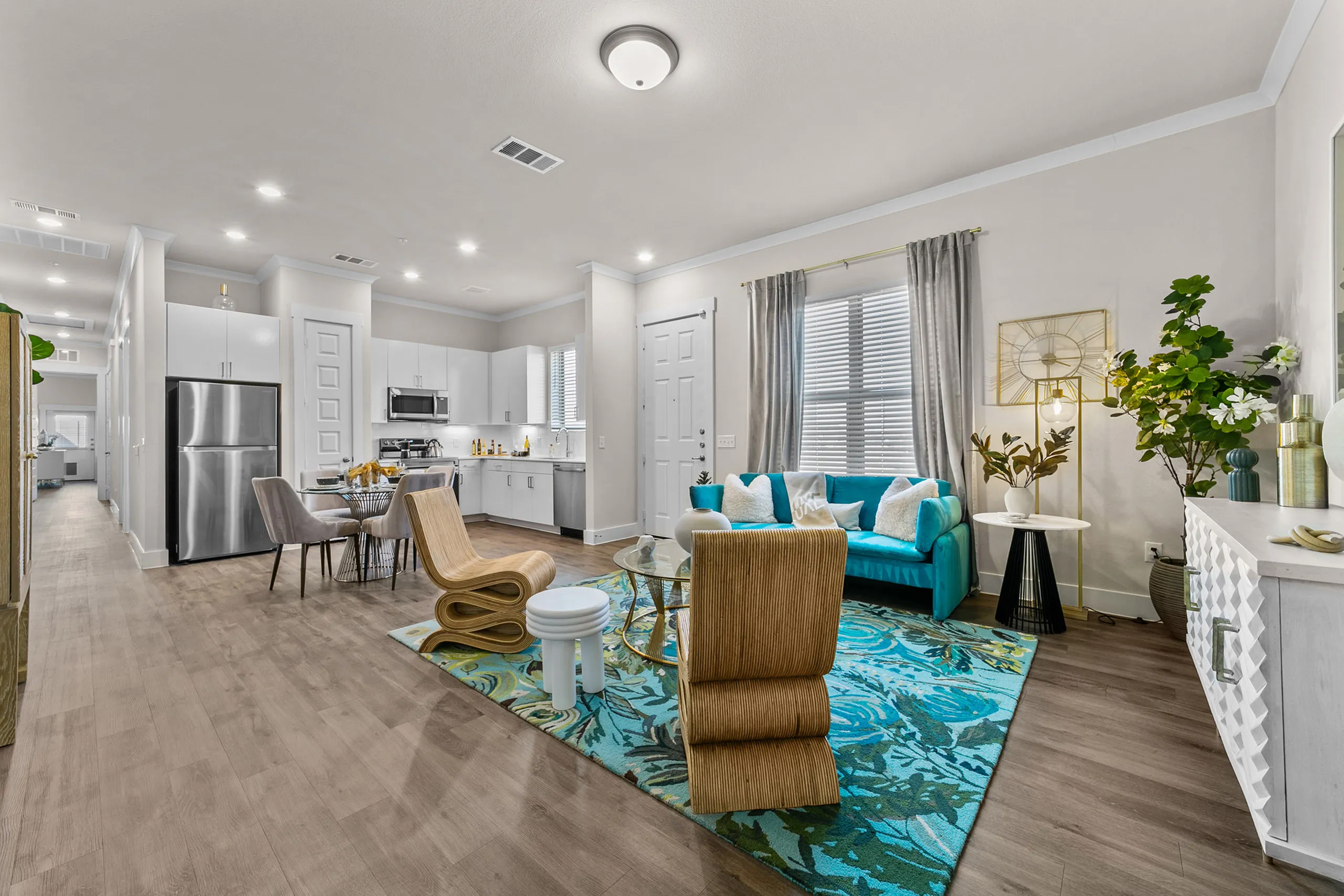 Modern open-concept living space with elegant furnishings, featuring a sleek kitchen, vibrant teal sofa, and stylish decor accents.