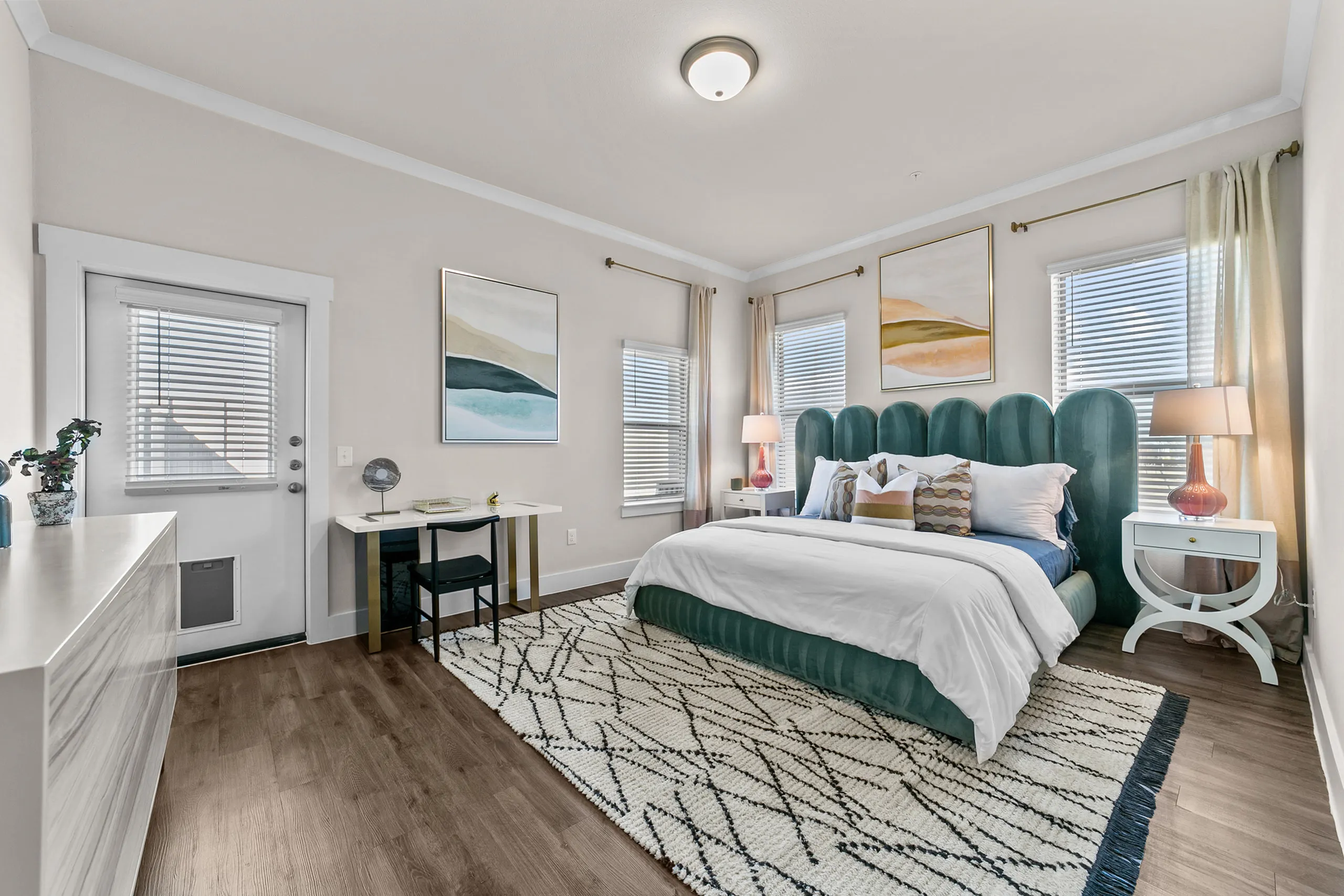 Bright and inviting bedroom with plush green headboard, stylish decor, and natural light streaming through large windows.