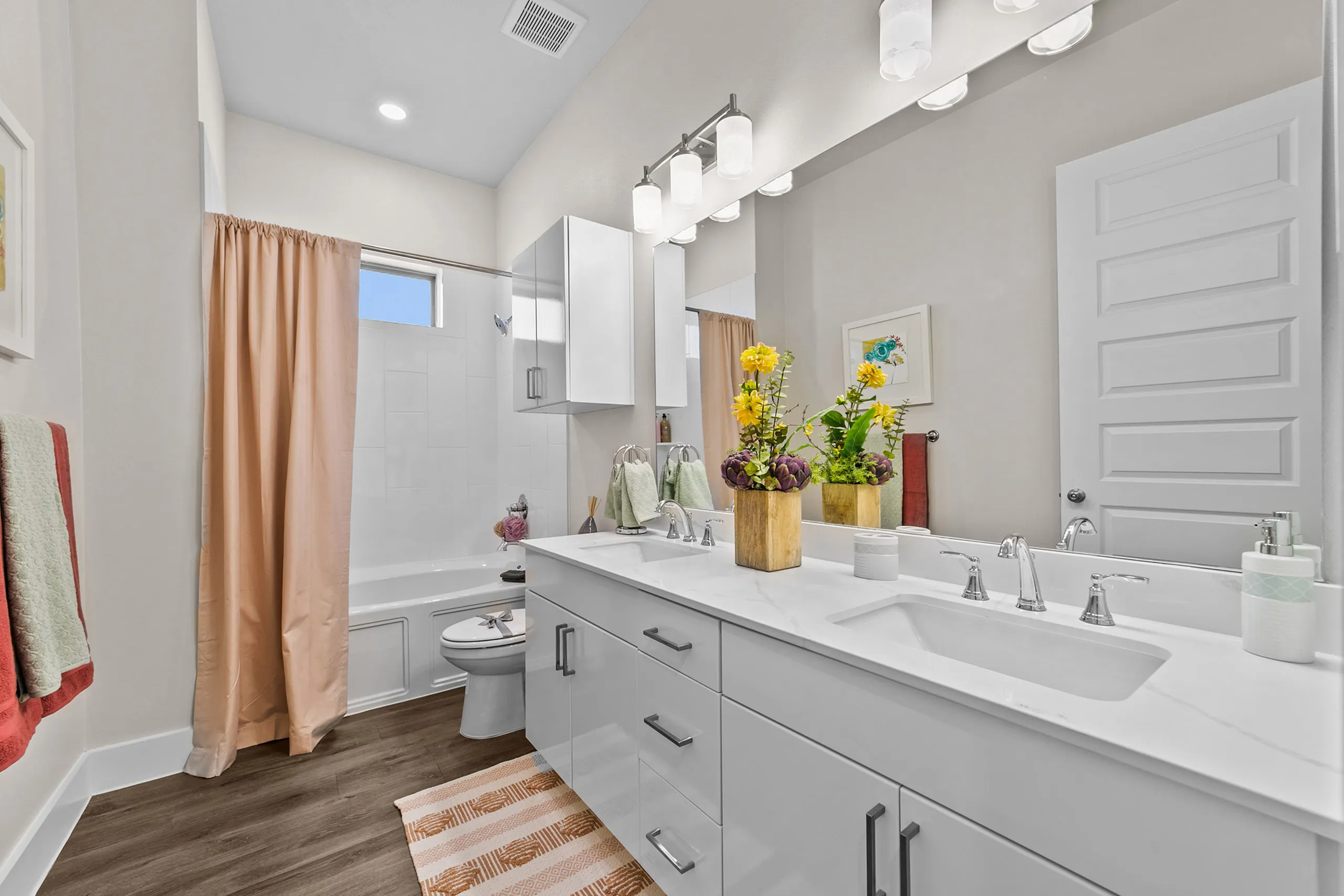 Elegant and bright bathroom featuring a sleek double vanity with modern fixtures, luxurious bathtub, and stylish decor with vibrant flowers.