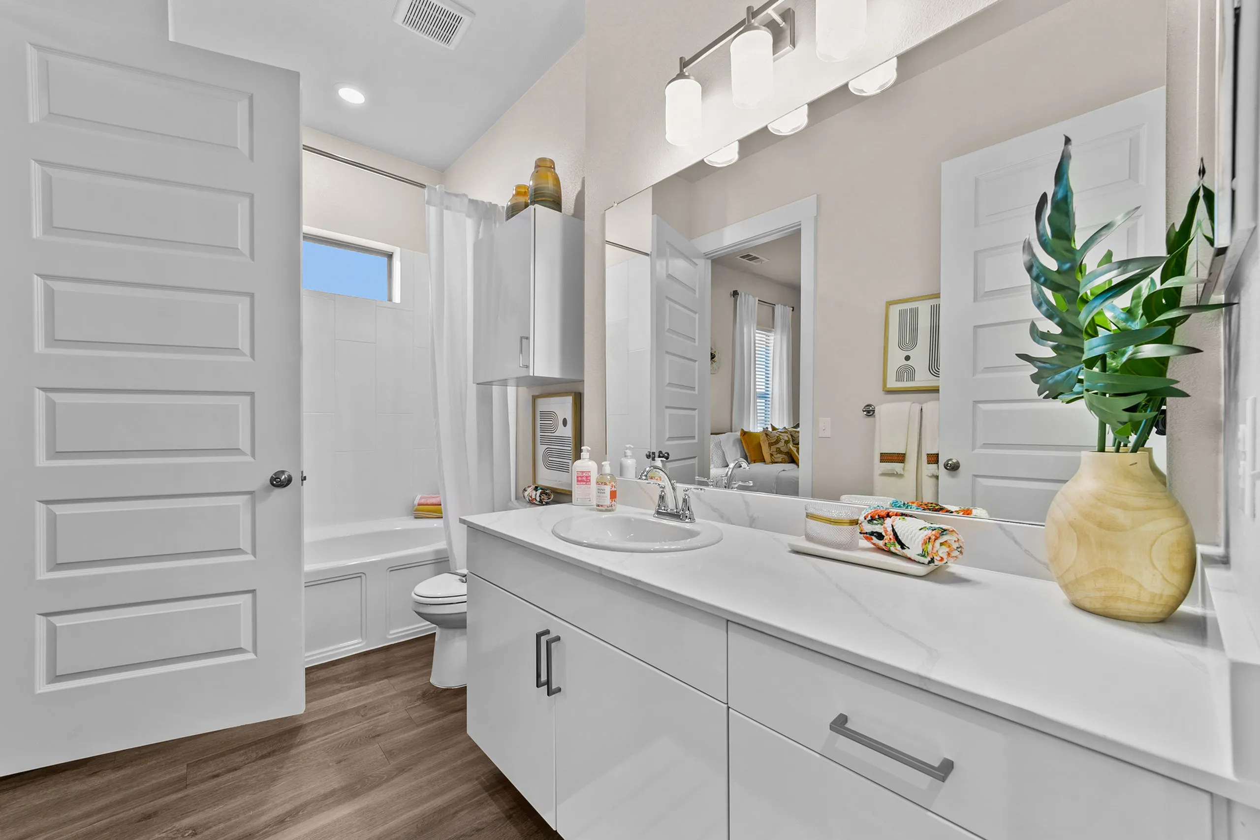 Modern and elegant bathroom featuring sleek white cabinets, a polished vanity with dual sinks, and sophisticated lighting, complemented by natural wood flooring.