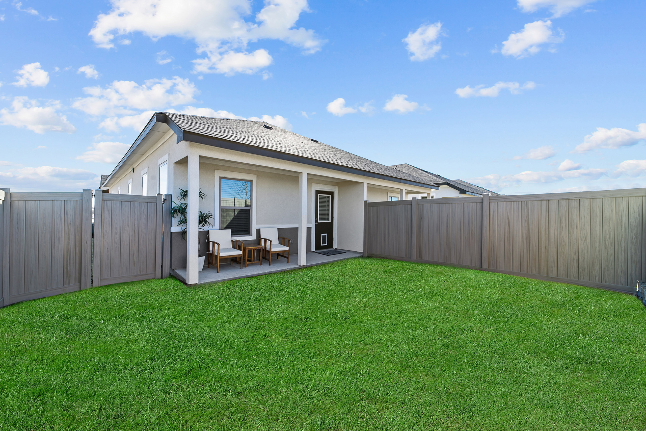 Charming backyard view featuring a cozy covered patio with stylish seating, enclosed by a modern fence under a clear blue sky.