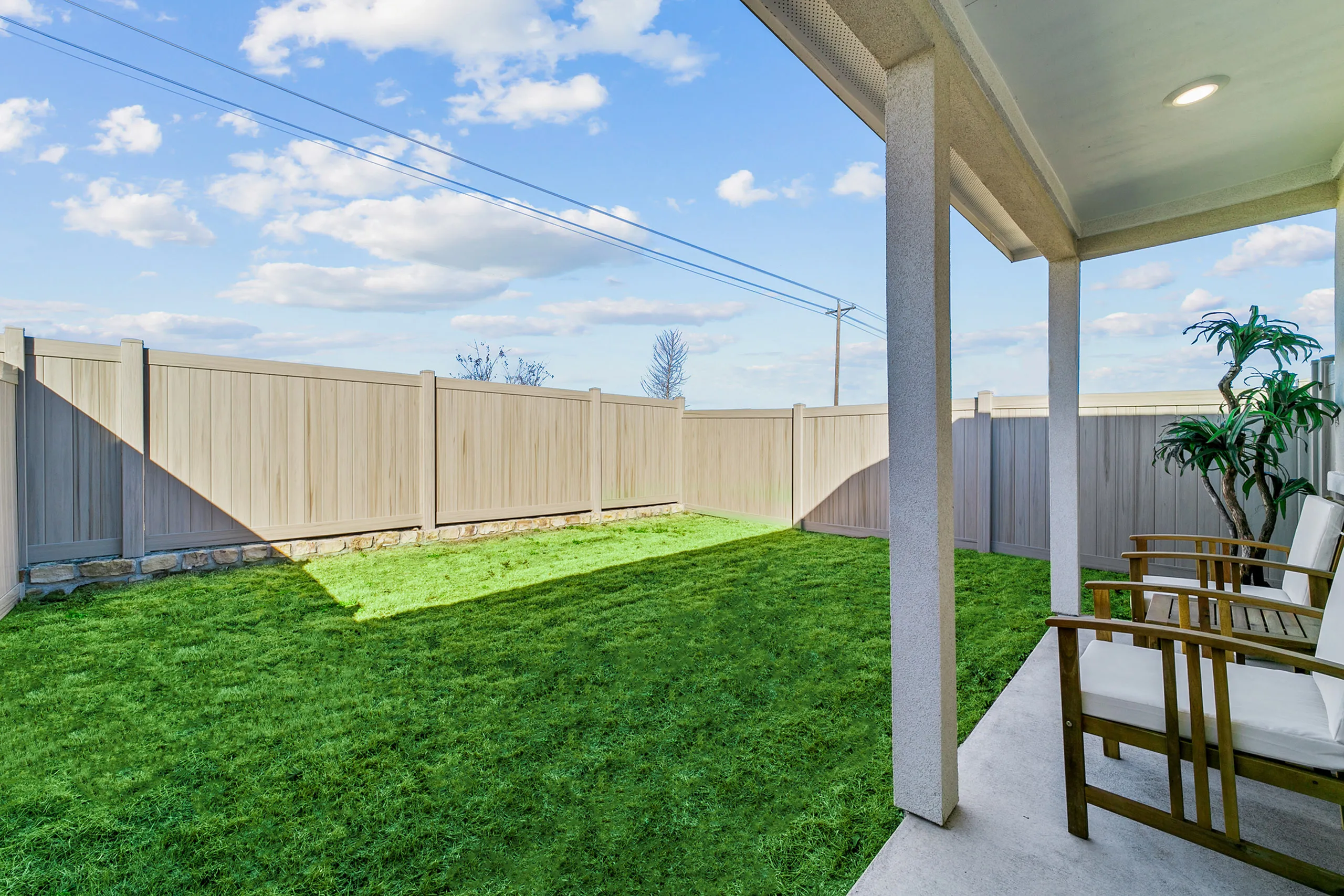 Charming backyard with lush green grass, a cozy patio, and stylish wooden chairs for outdoor relaxation.