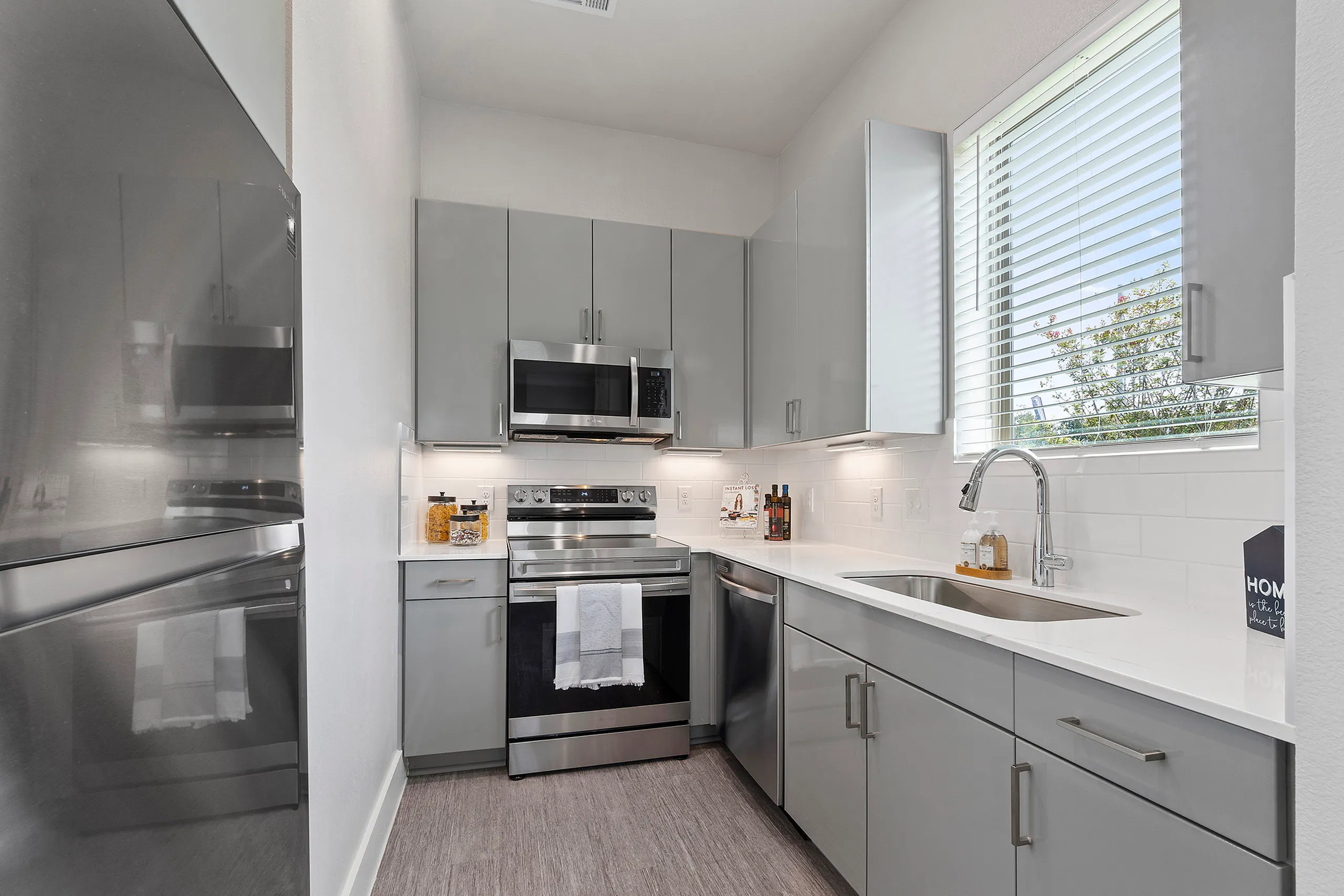 Modern kitchen with sleek gray cabinetry, stainless steel appliances, and ample natural light through a large window.