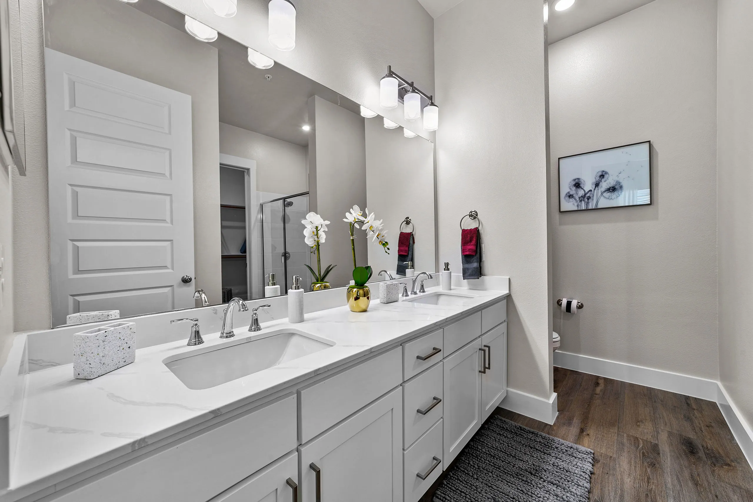 Elegant bathroom featuring a double vanity with chic white countertops, modern fixtures, and soft ambient lighting, complemented by stylish decor and hardwood flooring.