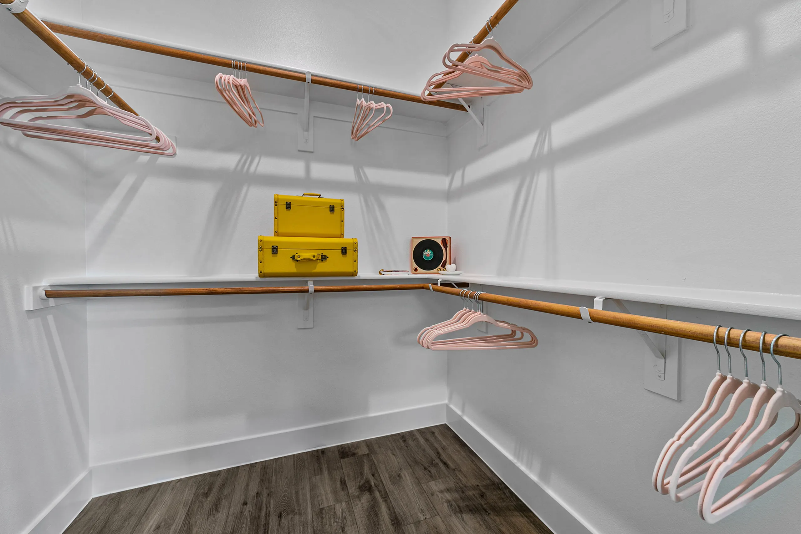 Spacious walk-in closet with elegant shelving and stylish hangers, featuring chic yellow storage boxes and a decorative vinyl record player on a wooden shelf.