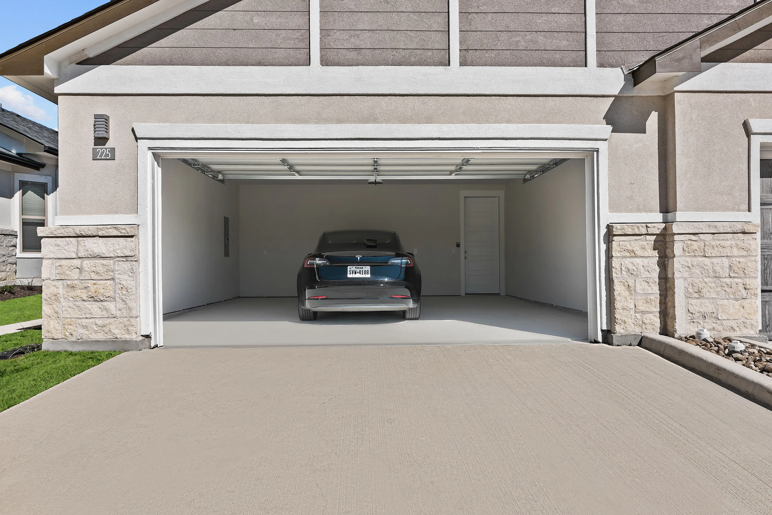 Modern home with spacious two-car garage featuring a sleek car parked, showcasing ample driveway space and contemporary design.