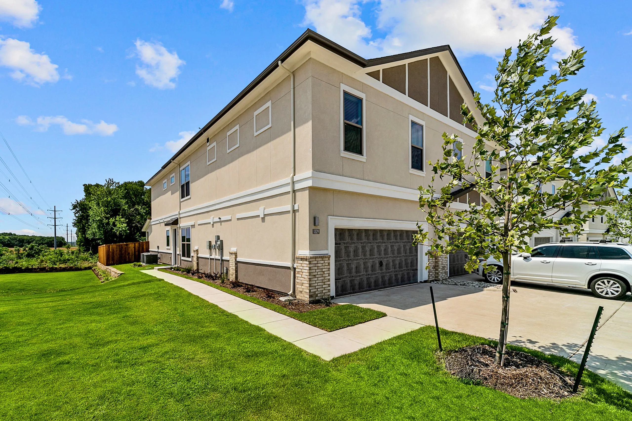 Modern townhouse with a sleek exterior, double garage, and lush green lawn under a clear blue sky.