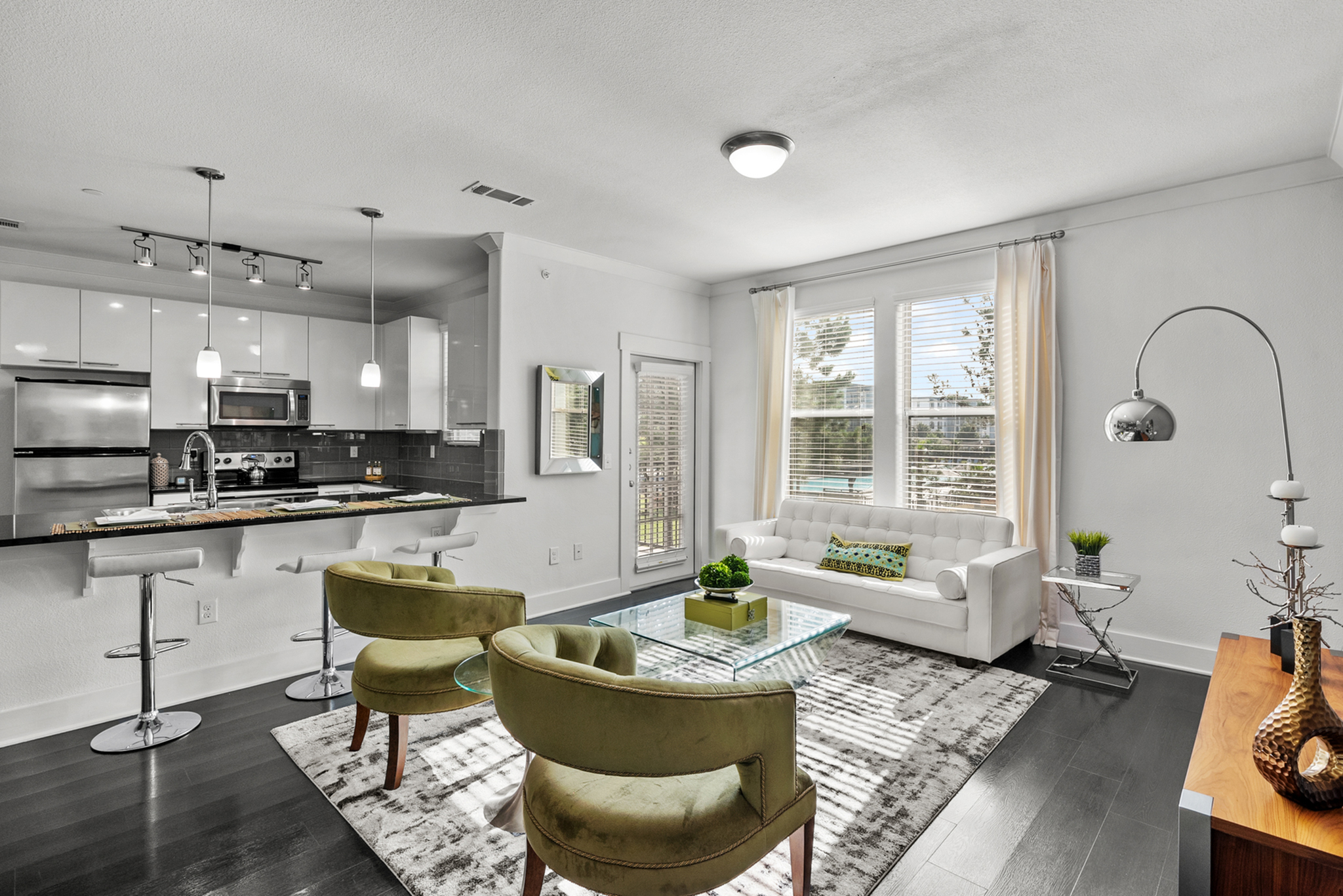 Modern open-concept living space with sleek kitchen, stylish bar seating, and cozy seating area featuring elegant armchairs and a plush sofa near expansive windows.