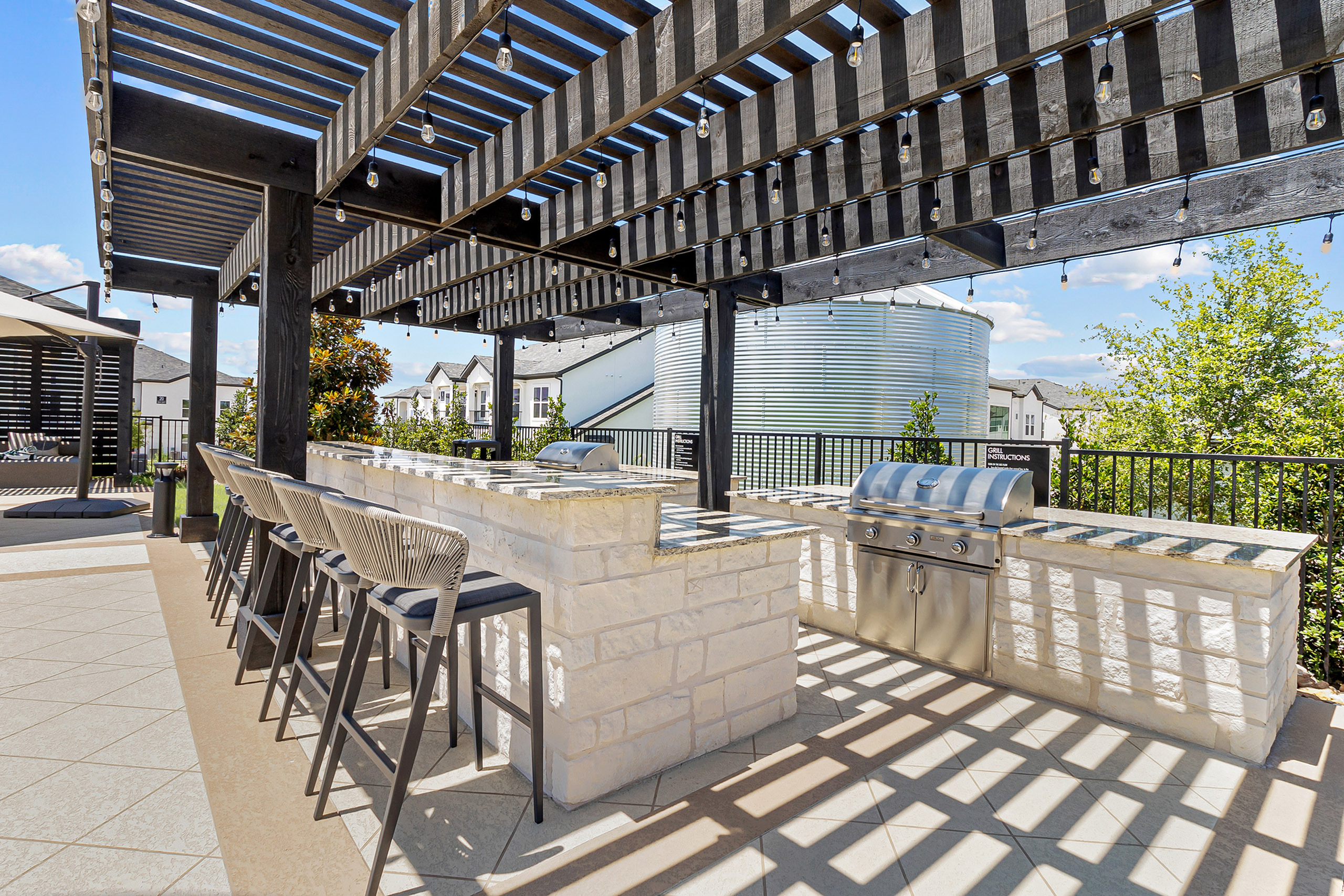 Chic outdoor kitchen with stylish seating and modern grill under wooden pergola, perfect for al fresco dining and entertaining.