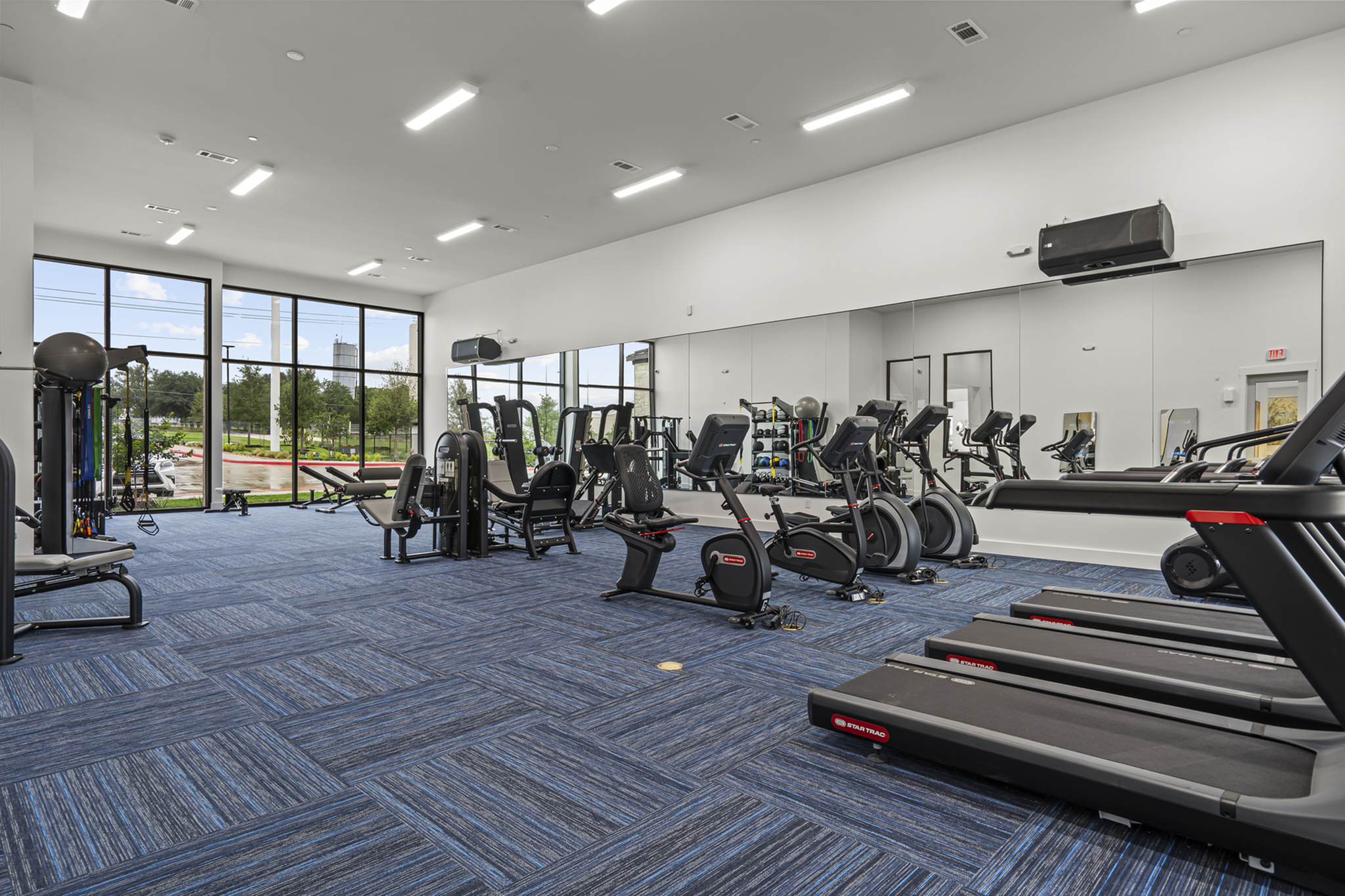 Modern fitness center with state-of-the-art equipment, large mirrors, and floor-to-ceiling windows showcasing scenic views.