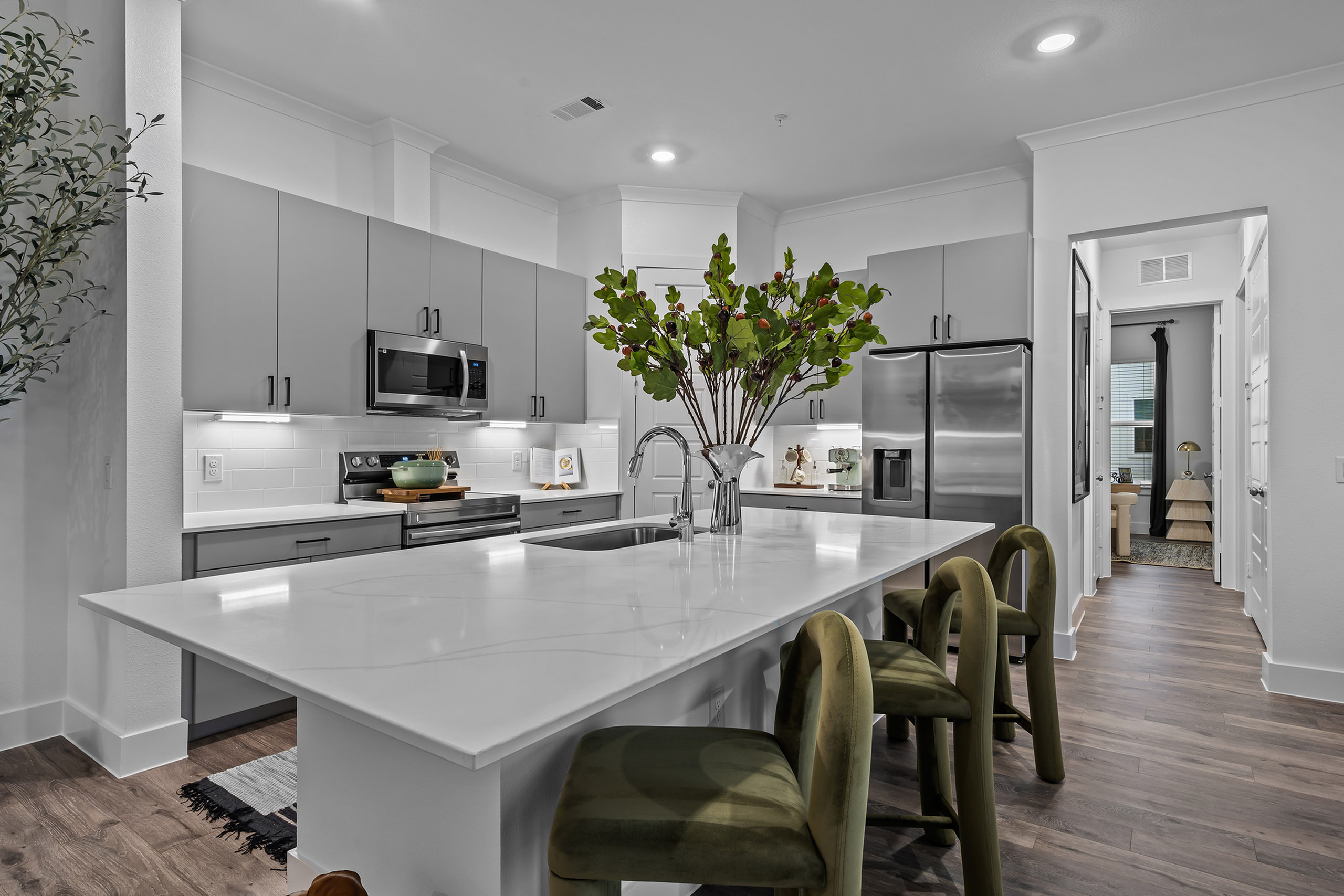 Modern kitchen with elegant white countertops, stainless steel appliances, and chic green bar stools, creating a sophisticated and inviting atmosphere.