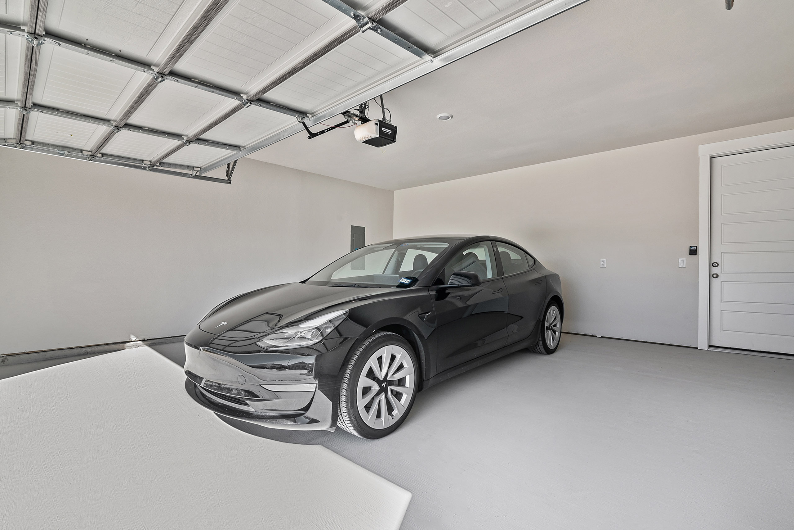 Modern garage interior showcasing a sleek black car parked on a pristine floor, highlighting ample space and contemporary design.